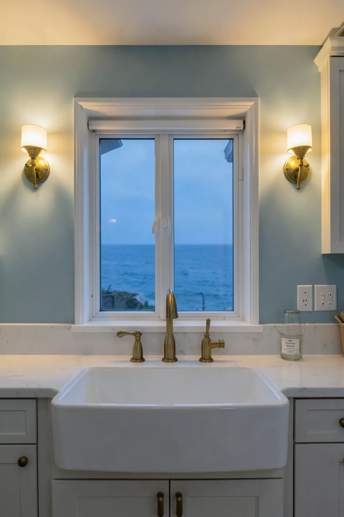 Warm antique brass sconces lighting up a soft blue wall in a coastal kitchen.