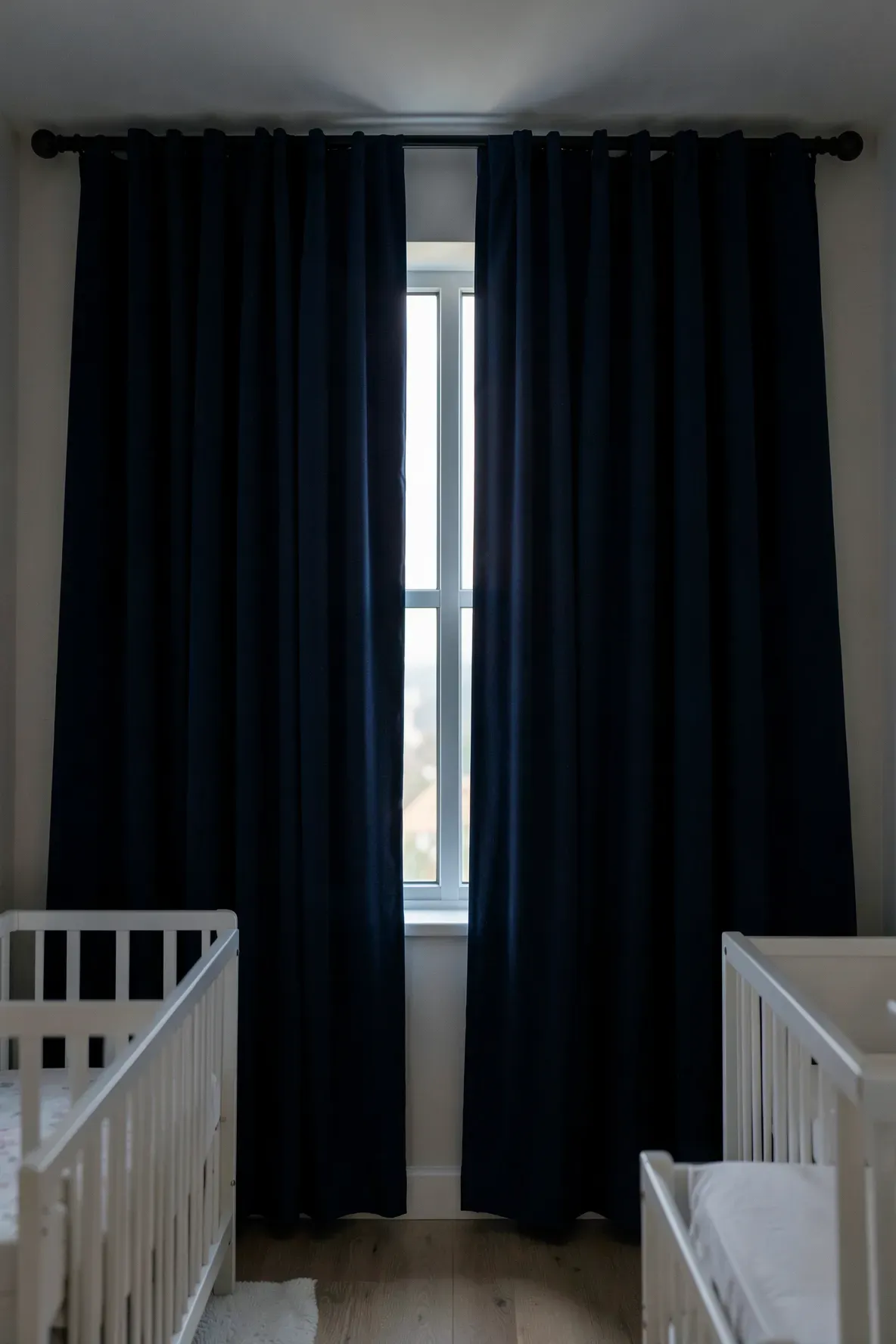 Heavy navy blue blackout curtains hanging from ceiling to floor in a quiet nursery.