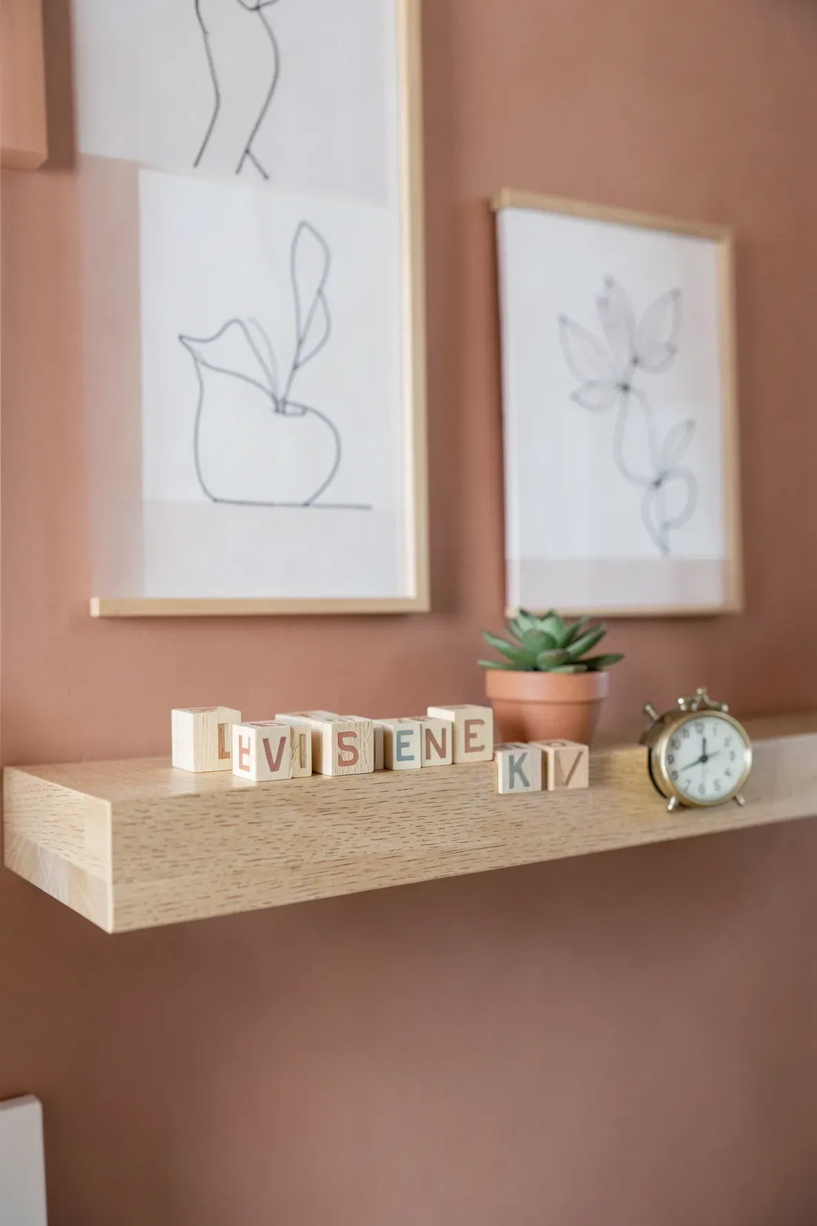 Classic wooden alphabet blocks arranged on a light oak shelf against a terracotta nursery wall.