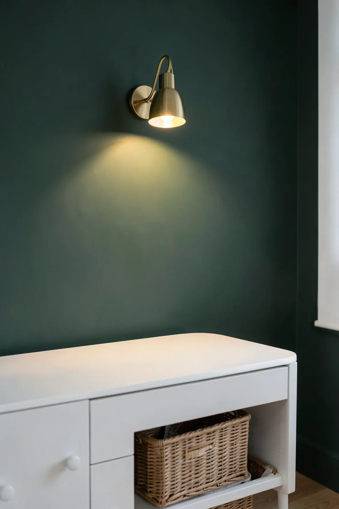A golden brass swing-arm wall lamp mounted above a white dresser in a nursery with a green wall.