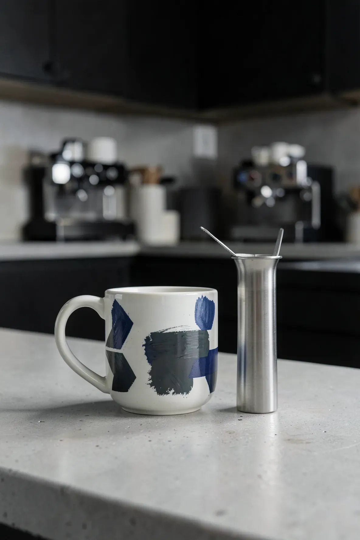 A hand-painted geometric pattern mug with a silver tea infuser inside on a gray countertop.