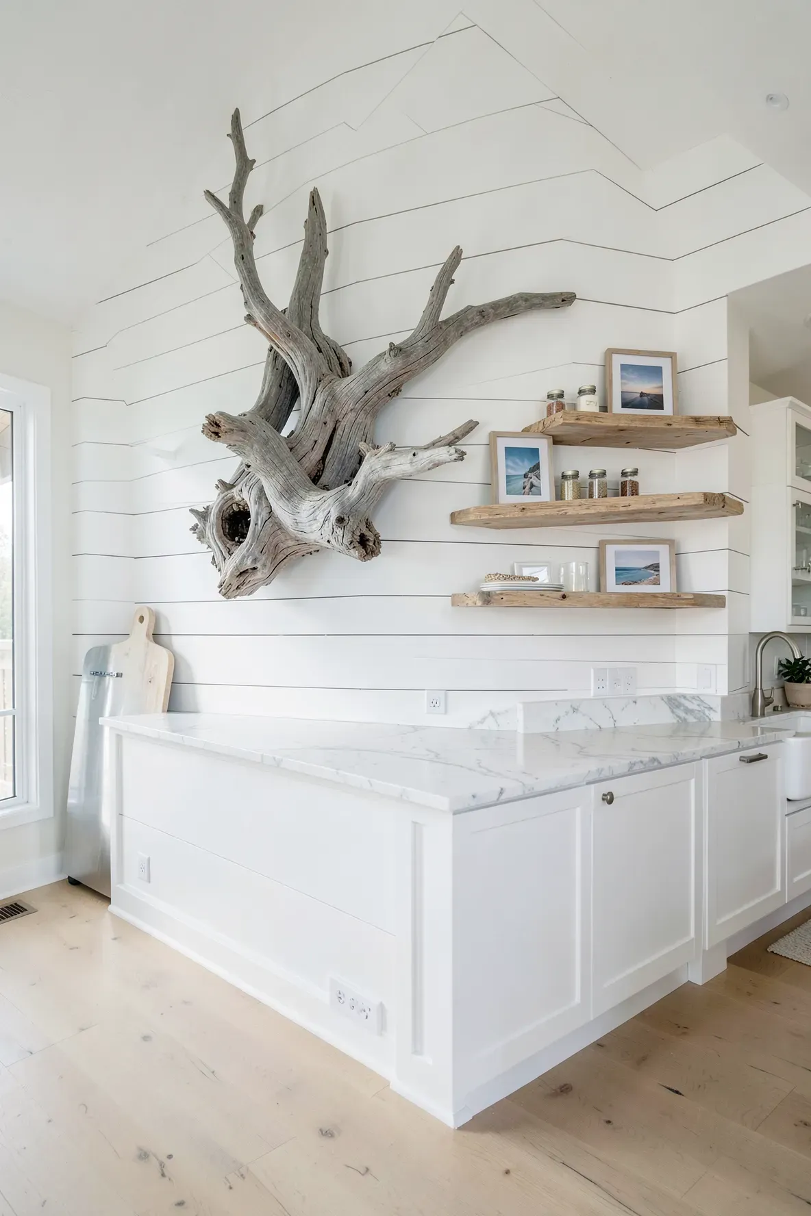 A large piece of gray driftwood and floating wood shelves on a white kitchen wall.