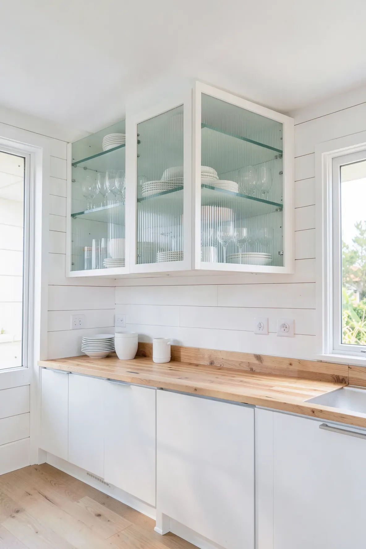 Modern coastal kitchen featuring glass-front upper cabinets and white shiplap walls.