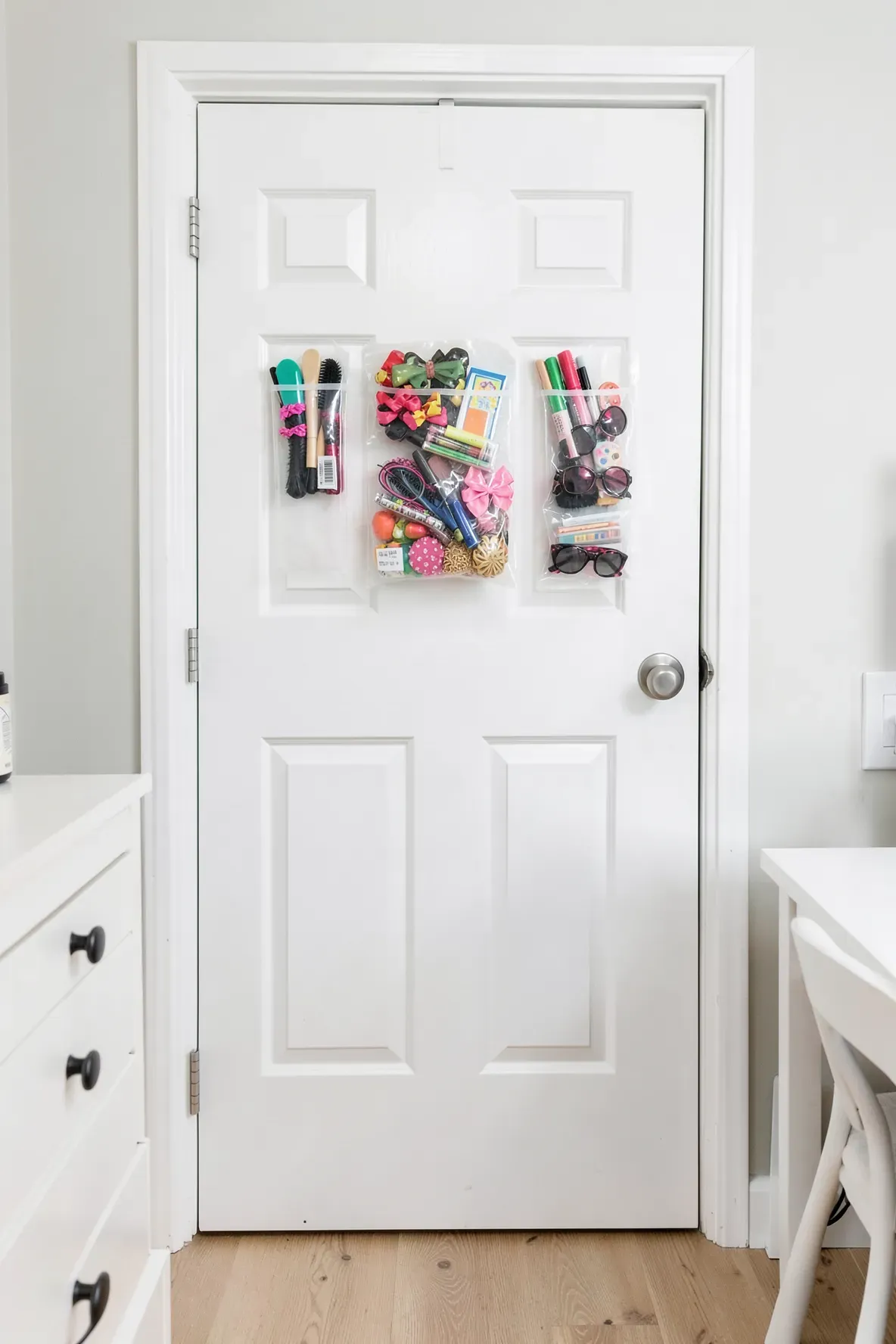 Clear hanging pocket organizer on a white door filled with colorful hair accessories and brushes.