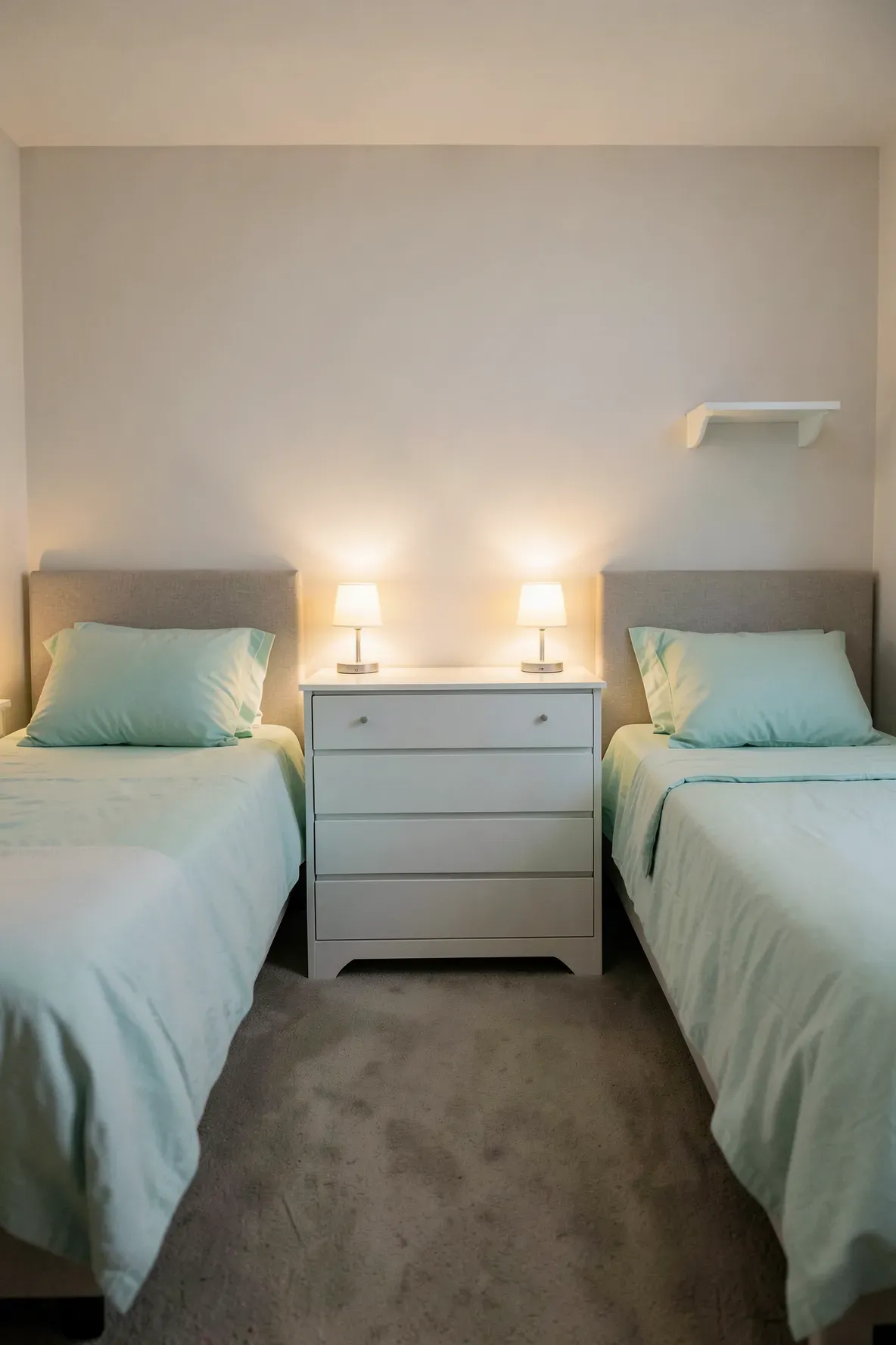 A white dresser placed between two twin beds serving as a shared nightstand with two lamps.