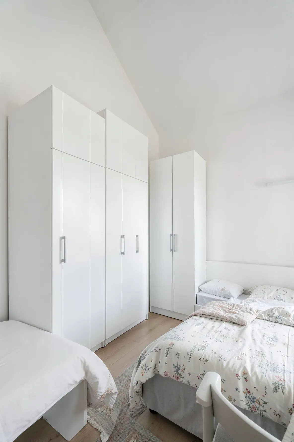 Tall, slim white armoires standing in the corners of a shared bedroom to save floor space.
