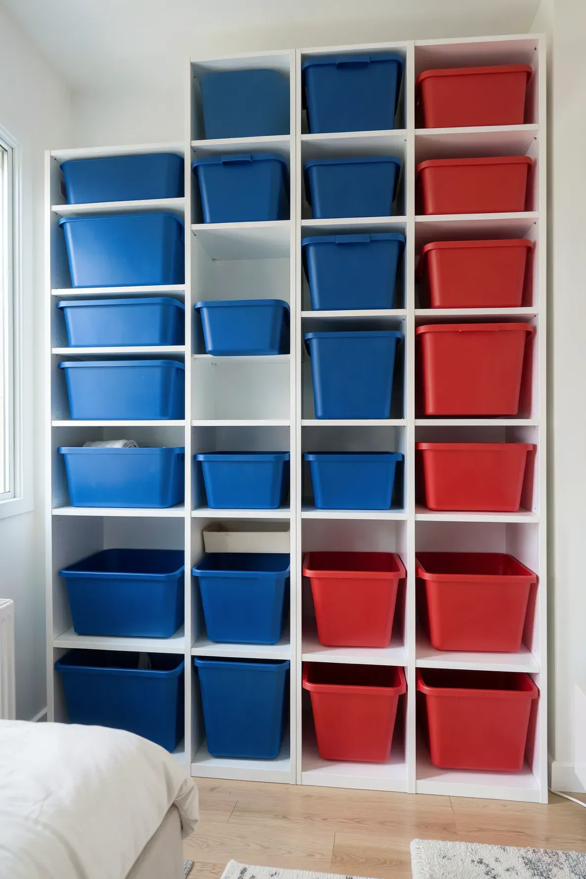 A white shelving unit with blue and red bins used for organized storage in a shared sibling room.