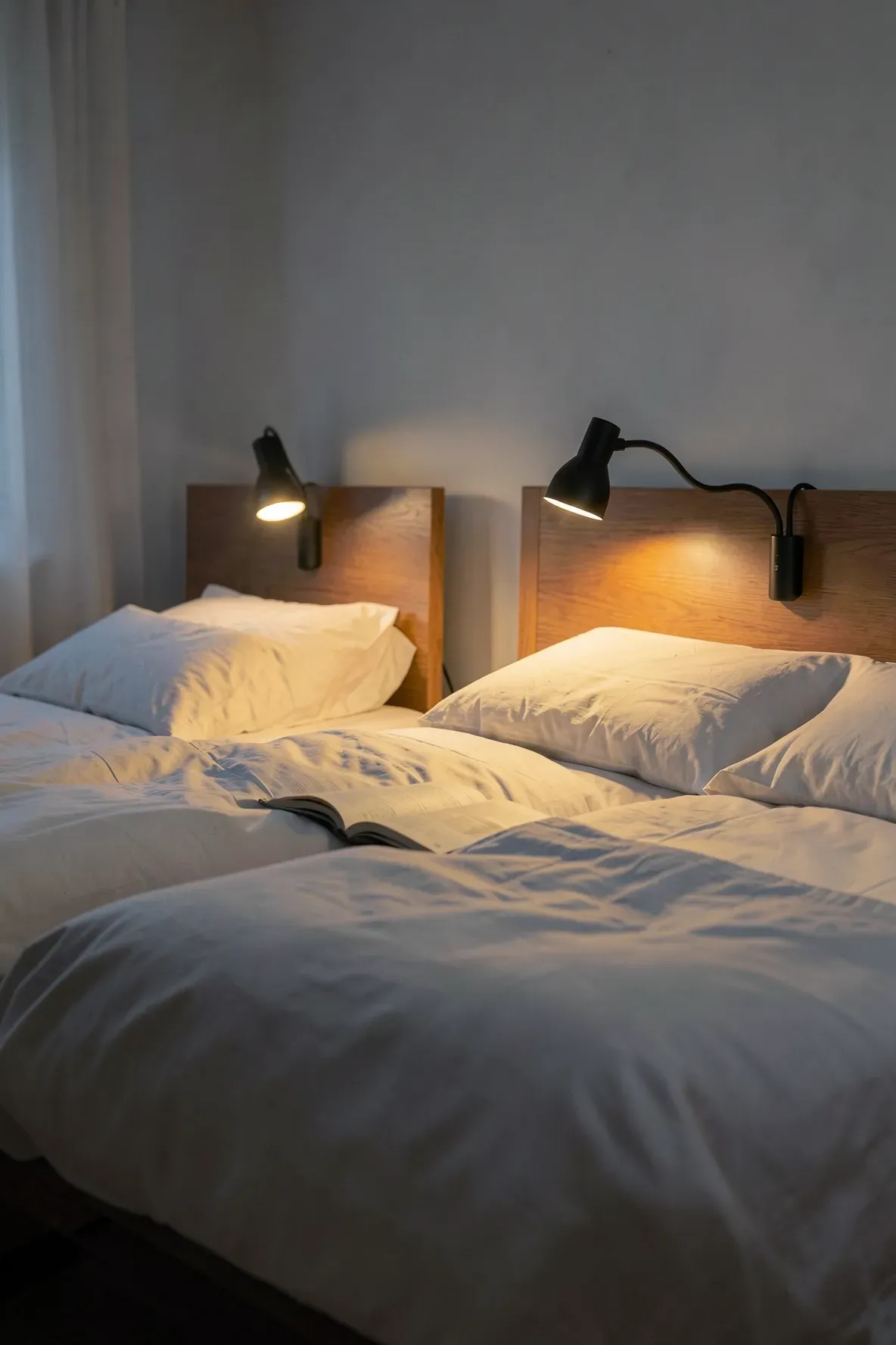Two beds in a shared room each equipped with its own flexible black reading lamp for private use.