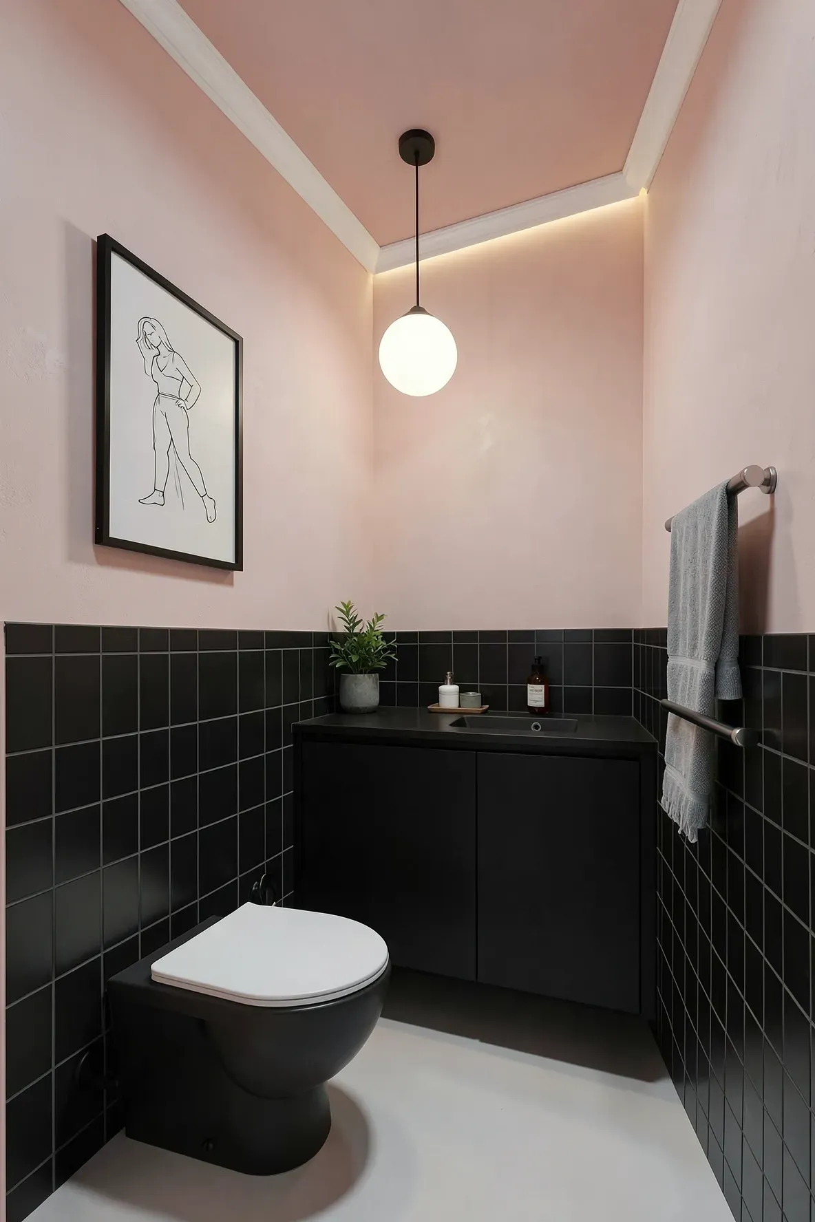 A modern corner bathroom with blush-pink walls and matte black tile base, a compact vanity and toilet in a tight layout, and a centered globe pendant light over the vanity with warm LED cove lighting around the ceiling perimeter.