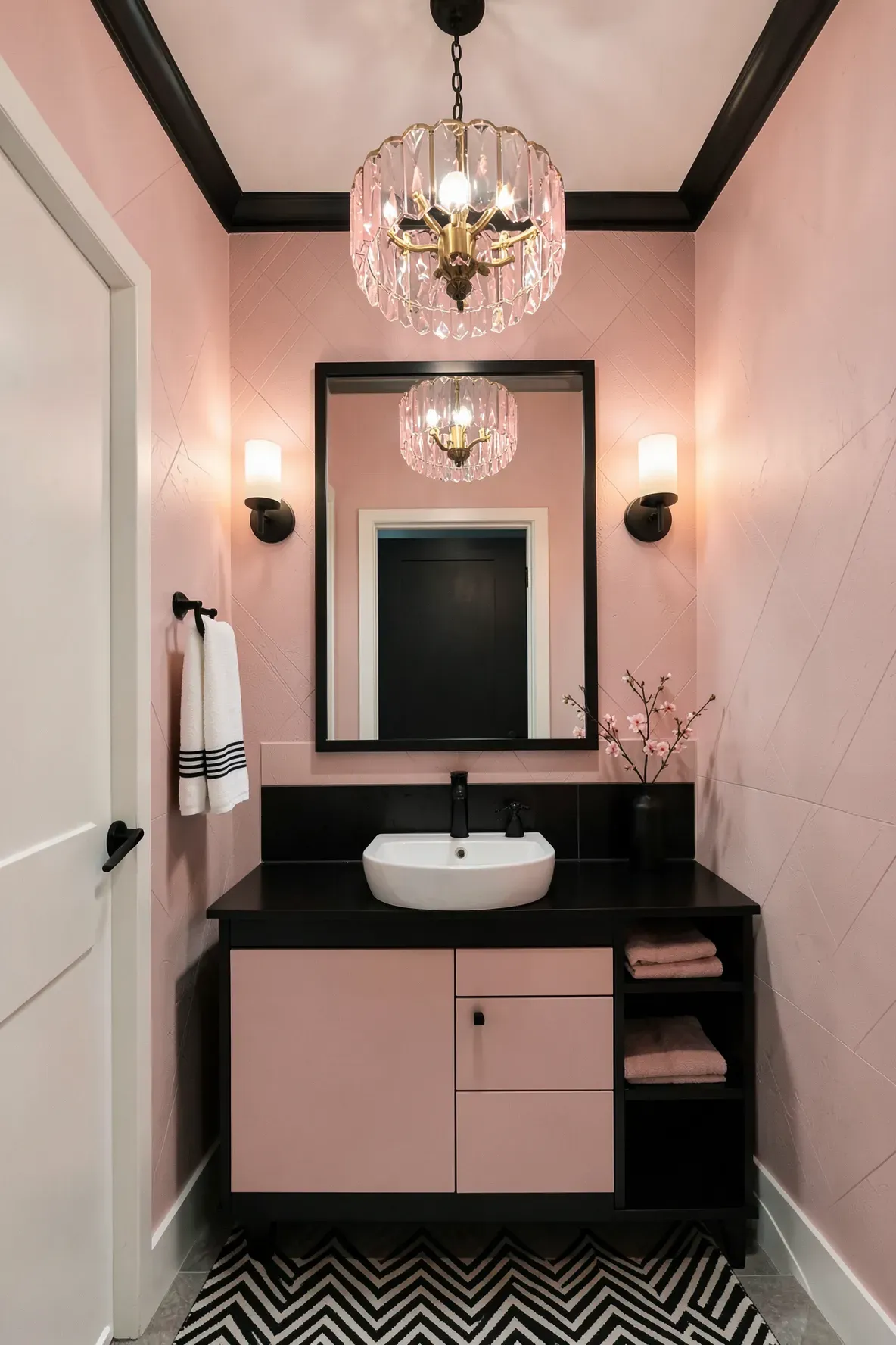 A small modern powder room with blush-pink walls, a thick black-framed mirror, a matte black vanity with a white vessel sink, a pink crystal drum chandelier above, warm sconces, a chevron rug, and neatly styled towels.