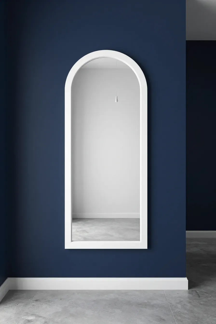 A minimalist white-framed arched mirror popping against a dark navy blue accent wall.