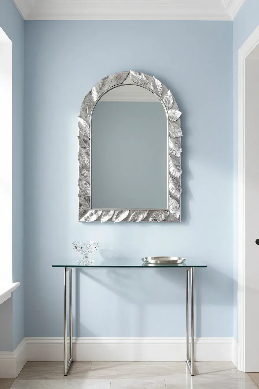 A shimmering silver leaf arched mirror hanging above a clear glass console table in a small foyer.