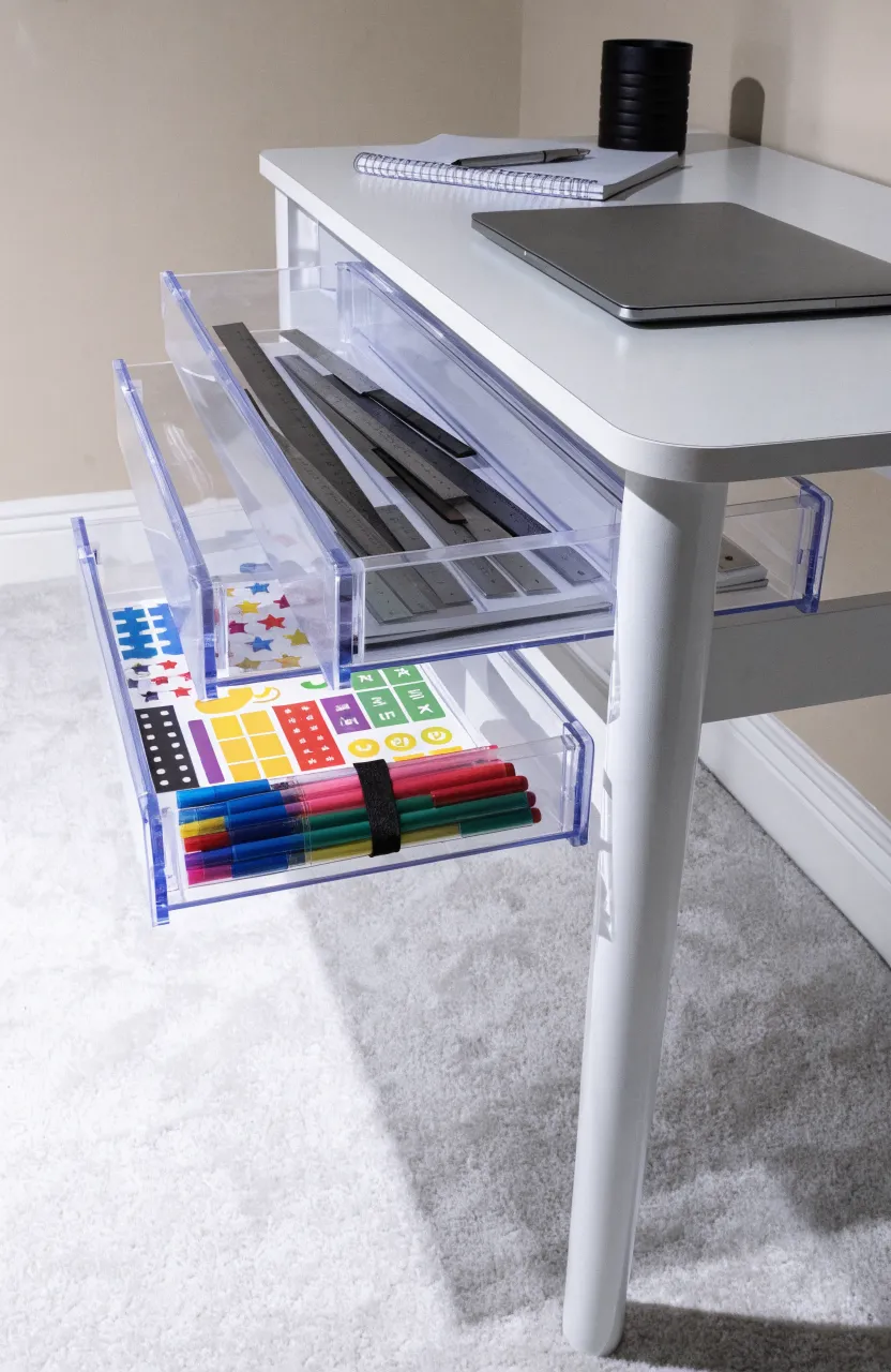 Clear plastic sliding drawers mounted under a white desk holding pens and craft supplies.