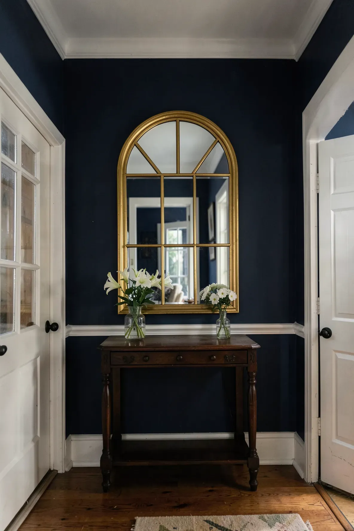 An arched gold mirror with a window-pane design hanging in a dark navy blue entryway.