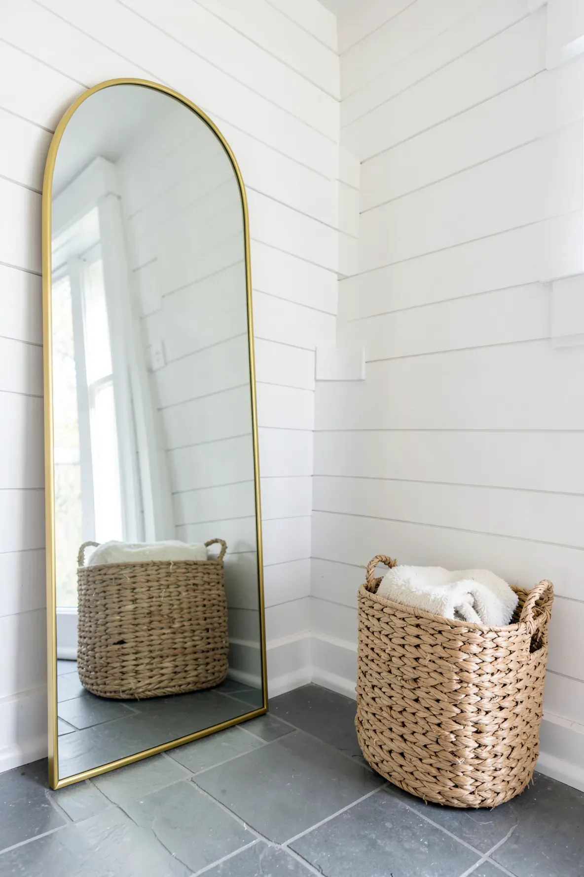 A large gold arch mirror leaning against a wall next to a large woven storage basket.
