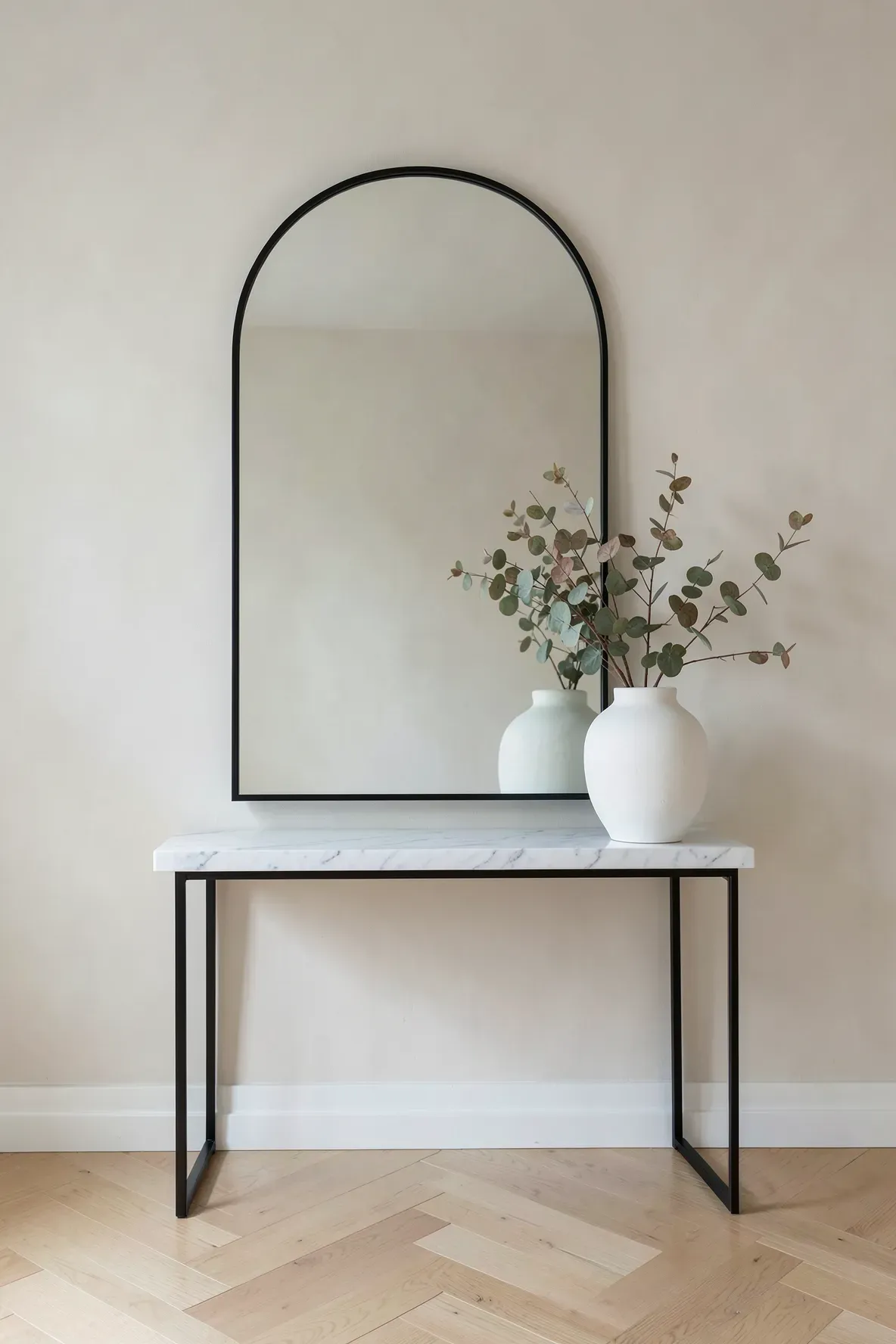 A thin black arched mirror on a white marble table with a single white ceramic vase.