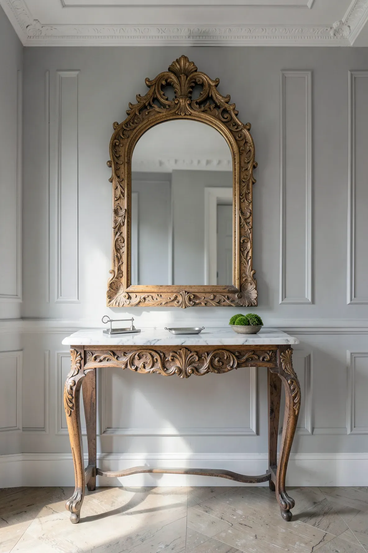 An intricately carved wood arched mirror above a white marble-topped entryway table.