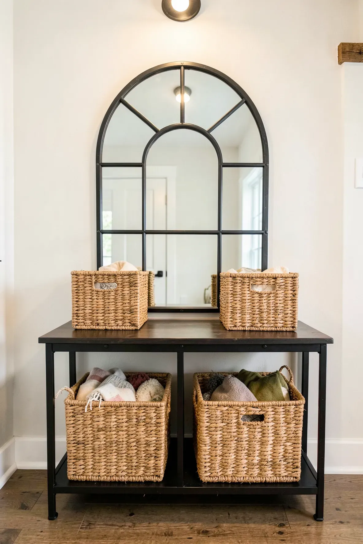 An industrial metal arched mirror above an entryway table with woven storage baskets underneath.