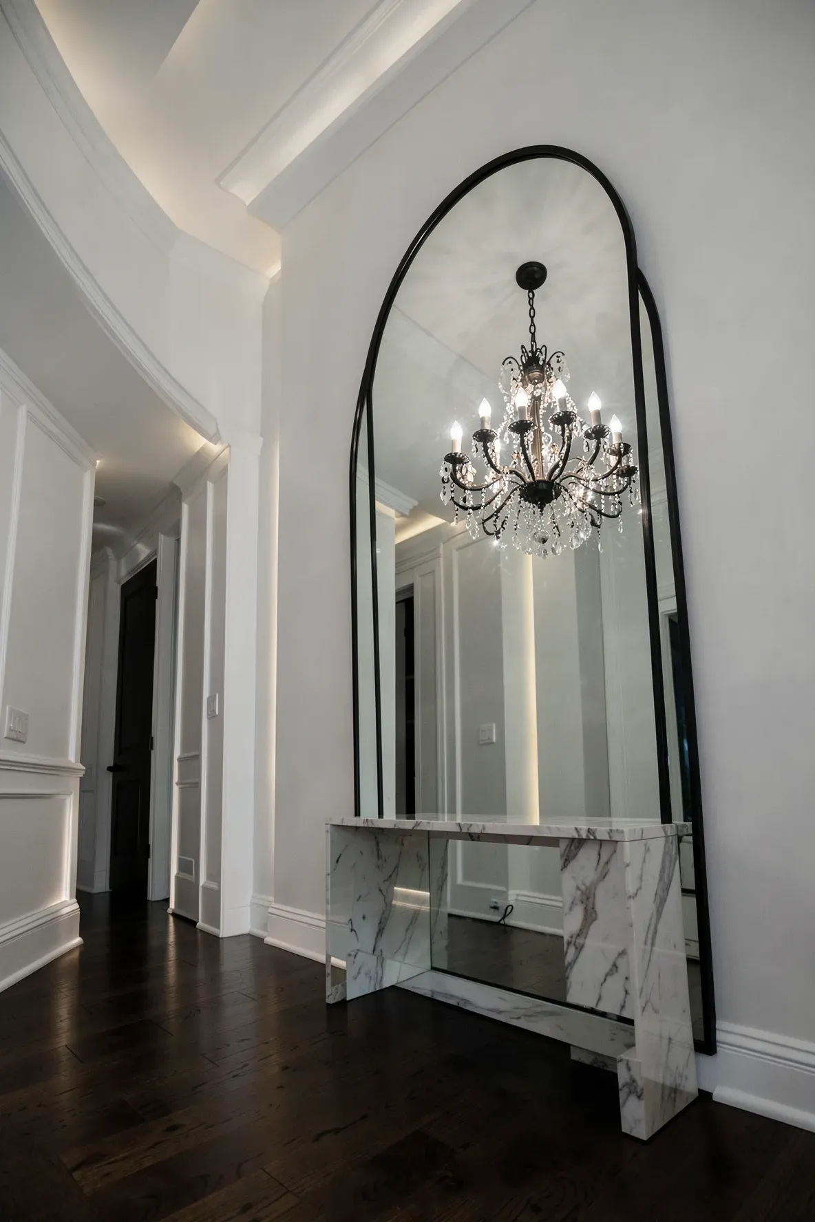 A large arched mirror reflecting a crystal chandelier in a luxury foyer with marble accents.