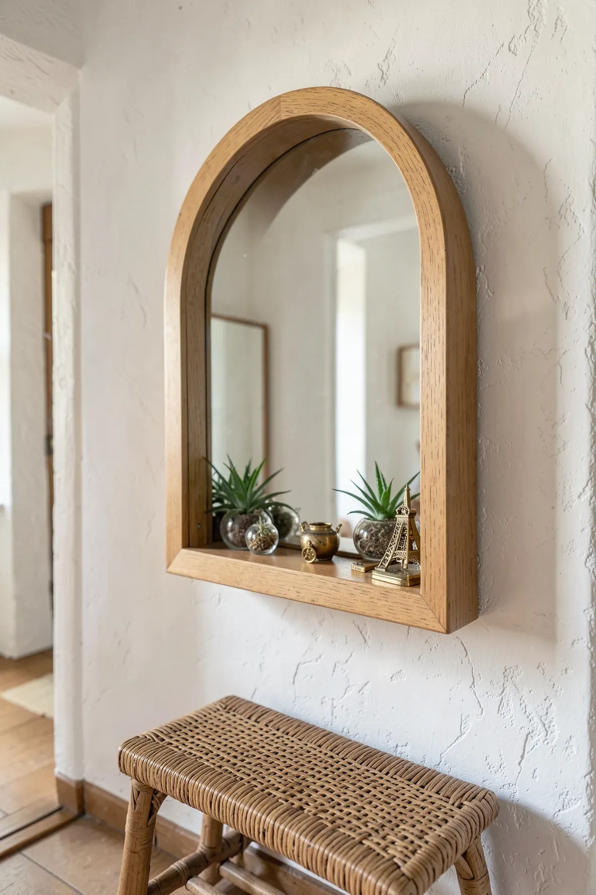 A deep-framed arched mirror holding small air plants and brass trinkets on its inner ledge.