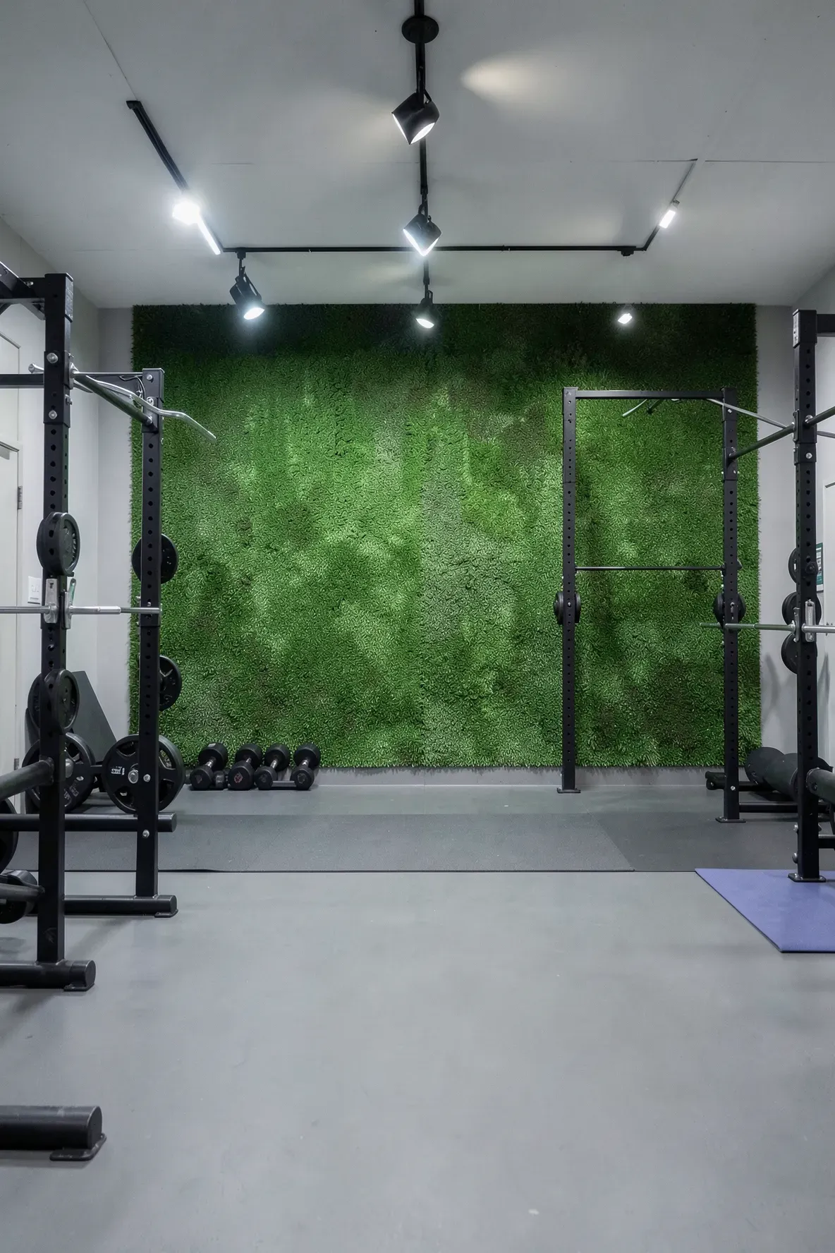 A modern basement gym featuring a vibrant green artificial grass accent wall behind exercise equipment.