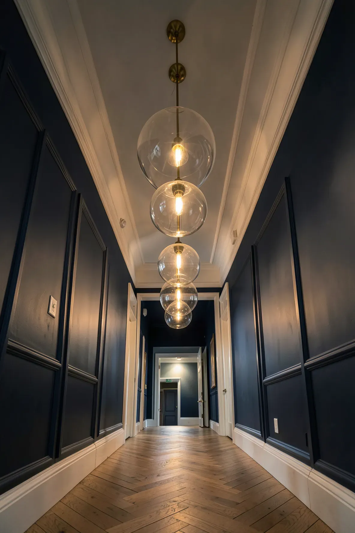 Large glass and brass pendant lights hanging from a high ceiling in a narrow navy hallway.