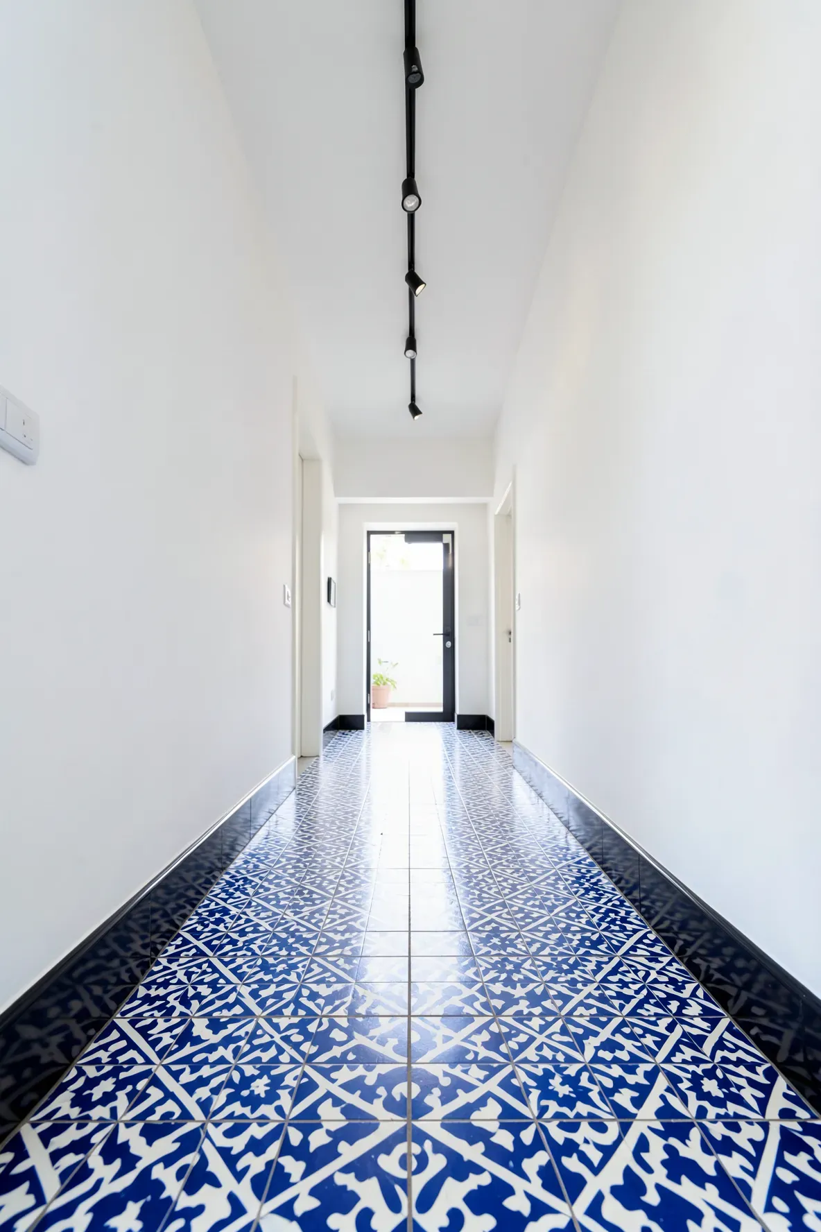 A narrow hallway with striking blue and white patterned floor tiles and clean white walls.