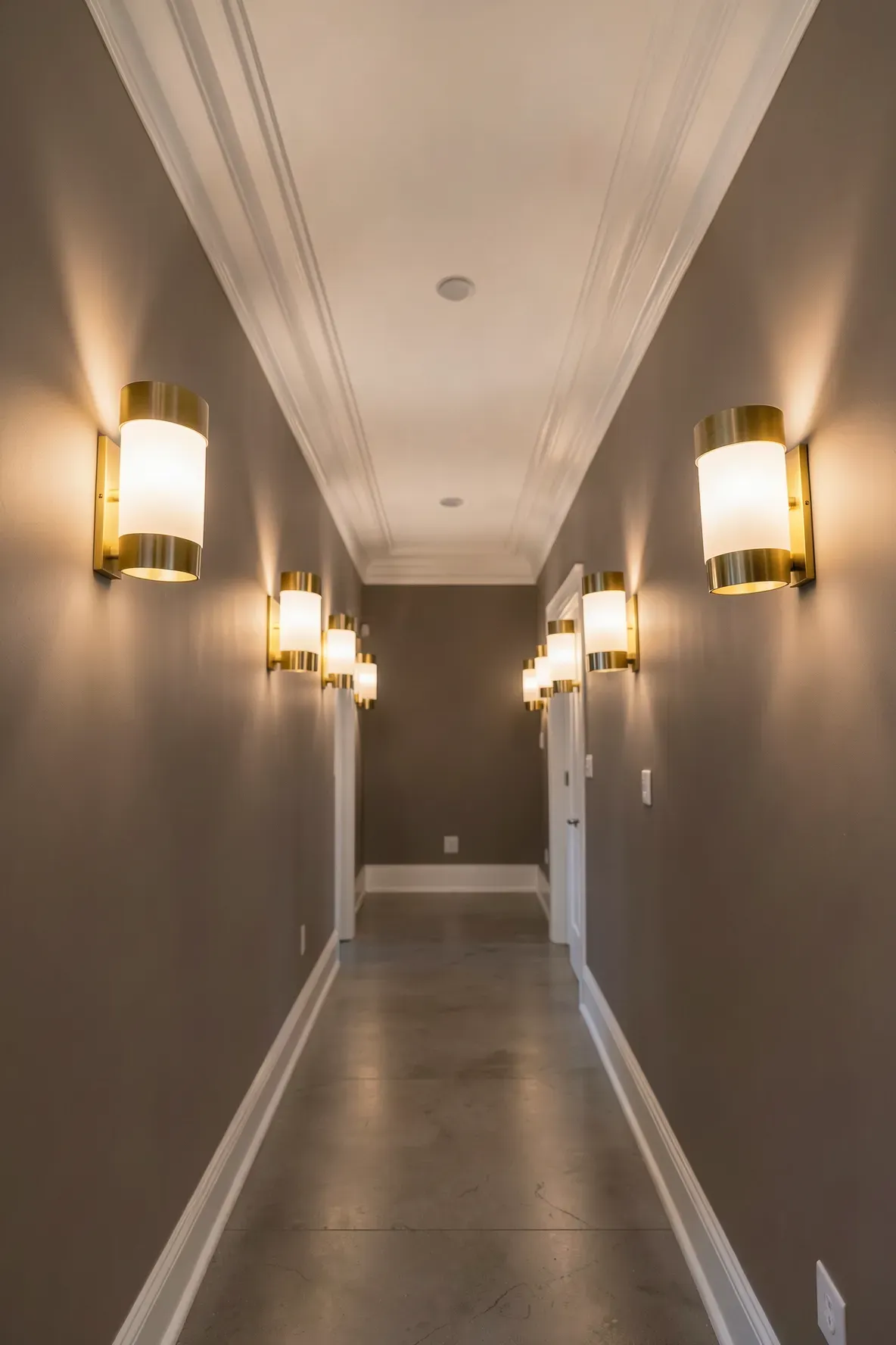A long narrow hallway with several matching brass wall sconces providing warm, rhythmic lighting.