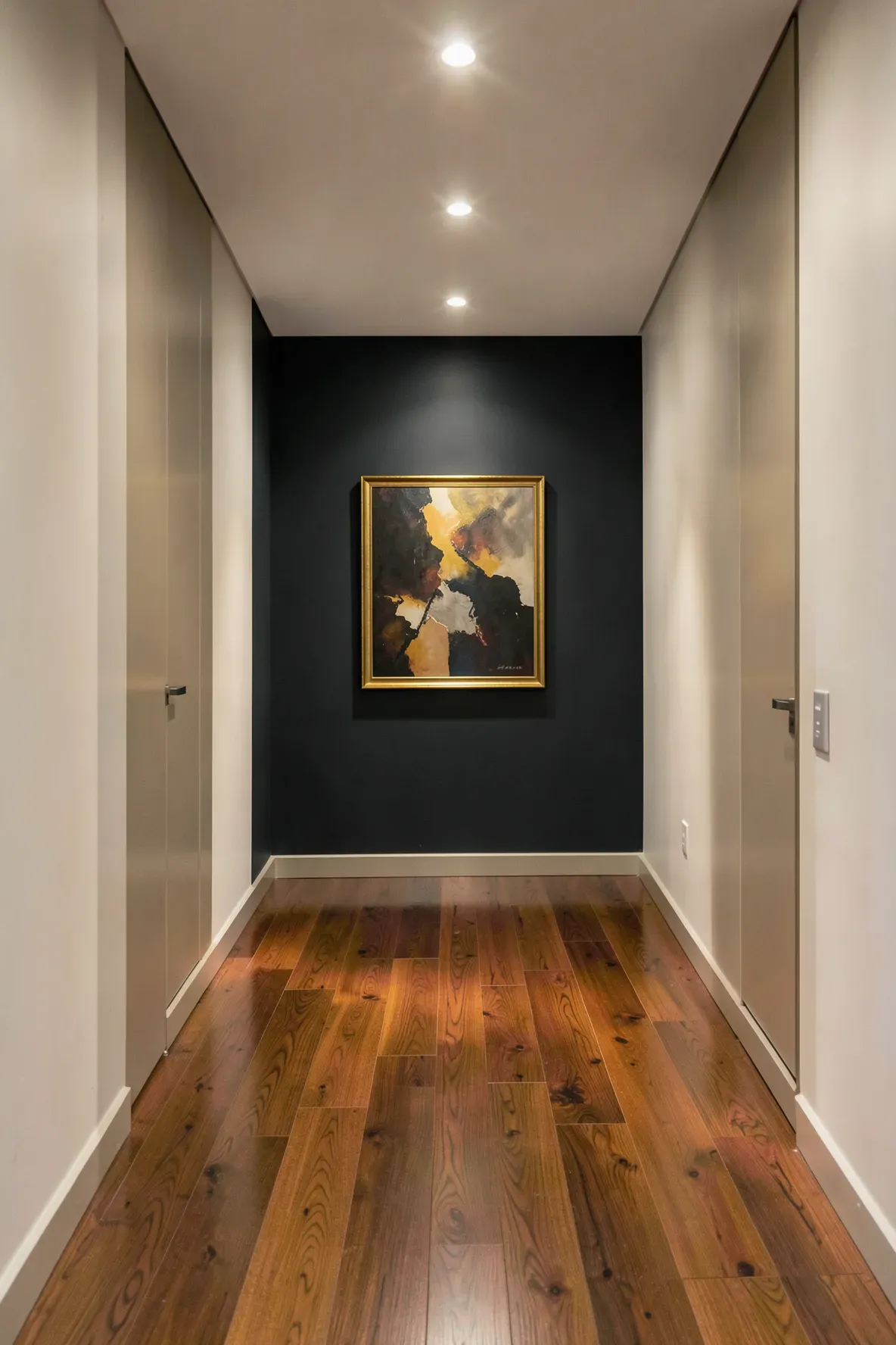A long hallway with white side walls leading to a dark charcoal accent wall with art.