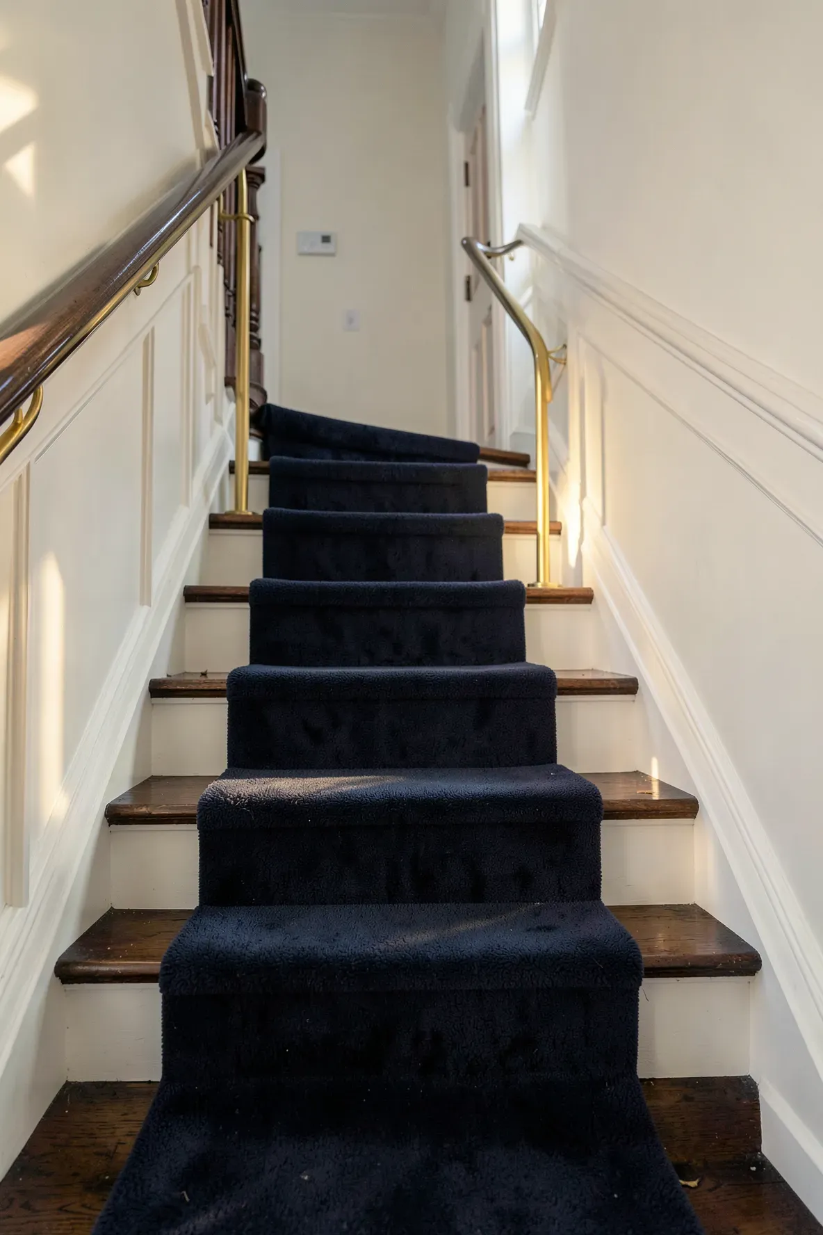 A navy blue stair runner with gold metallic rods in a traditional narrow entryway.