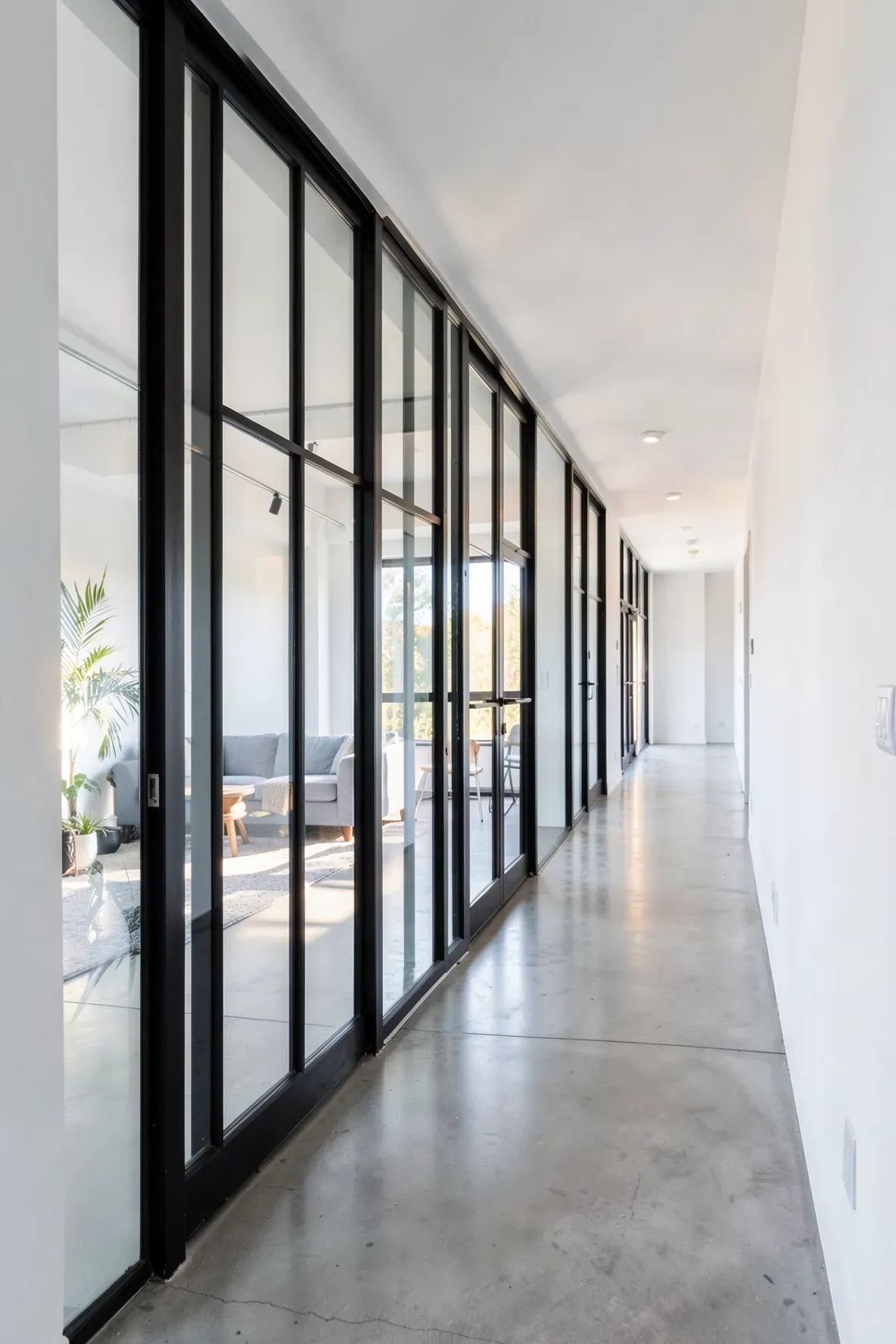 Black-framed glass doors allowing light to flow into a narrow modern hallway.