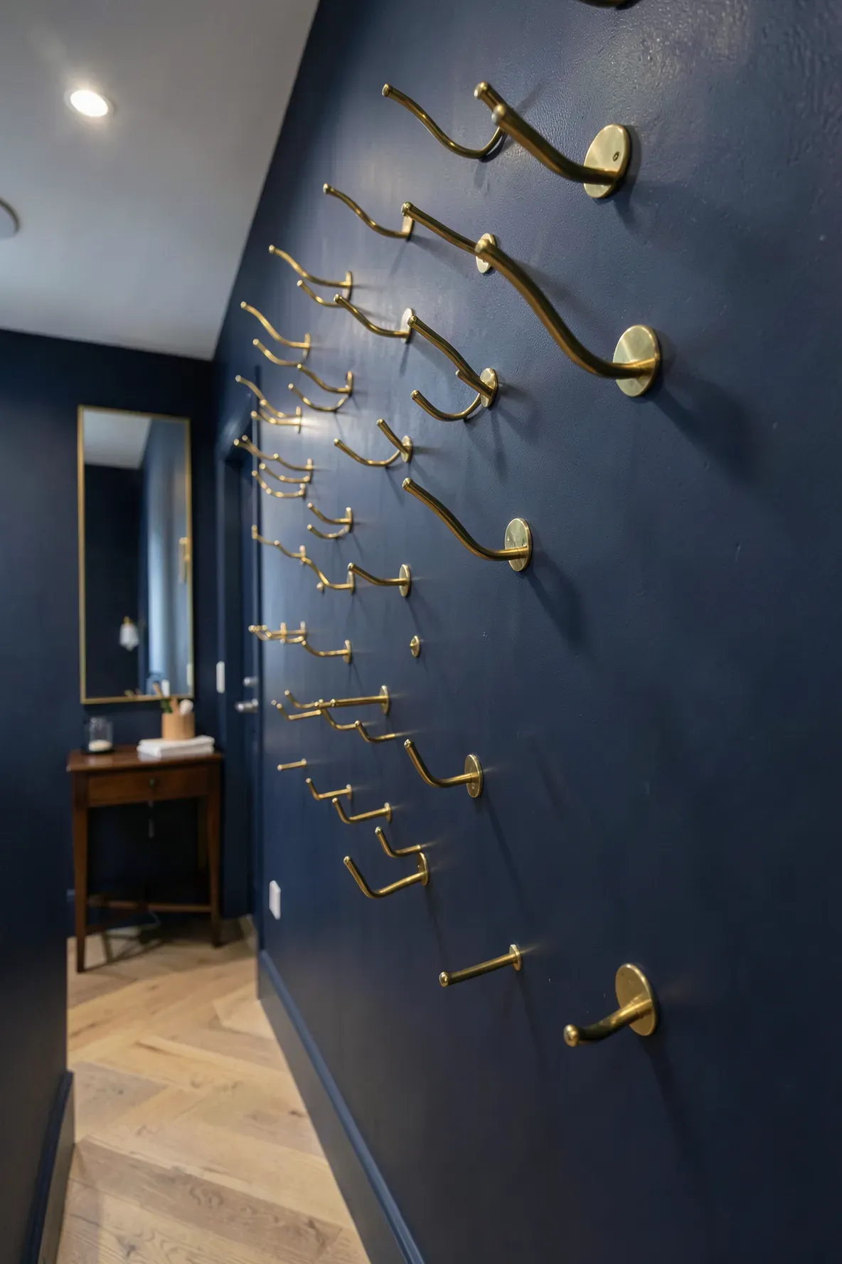 Polished brass hooks arranged at different heights on a navy blue hallway wall.