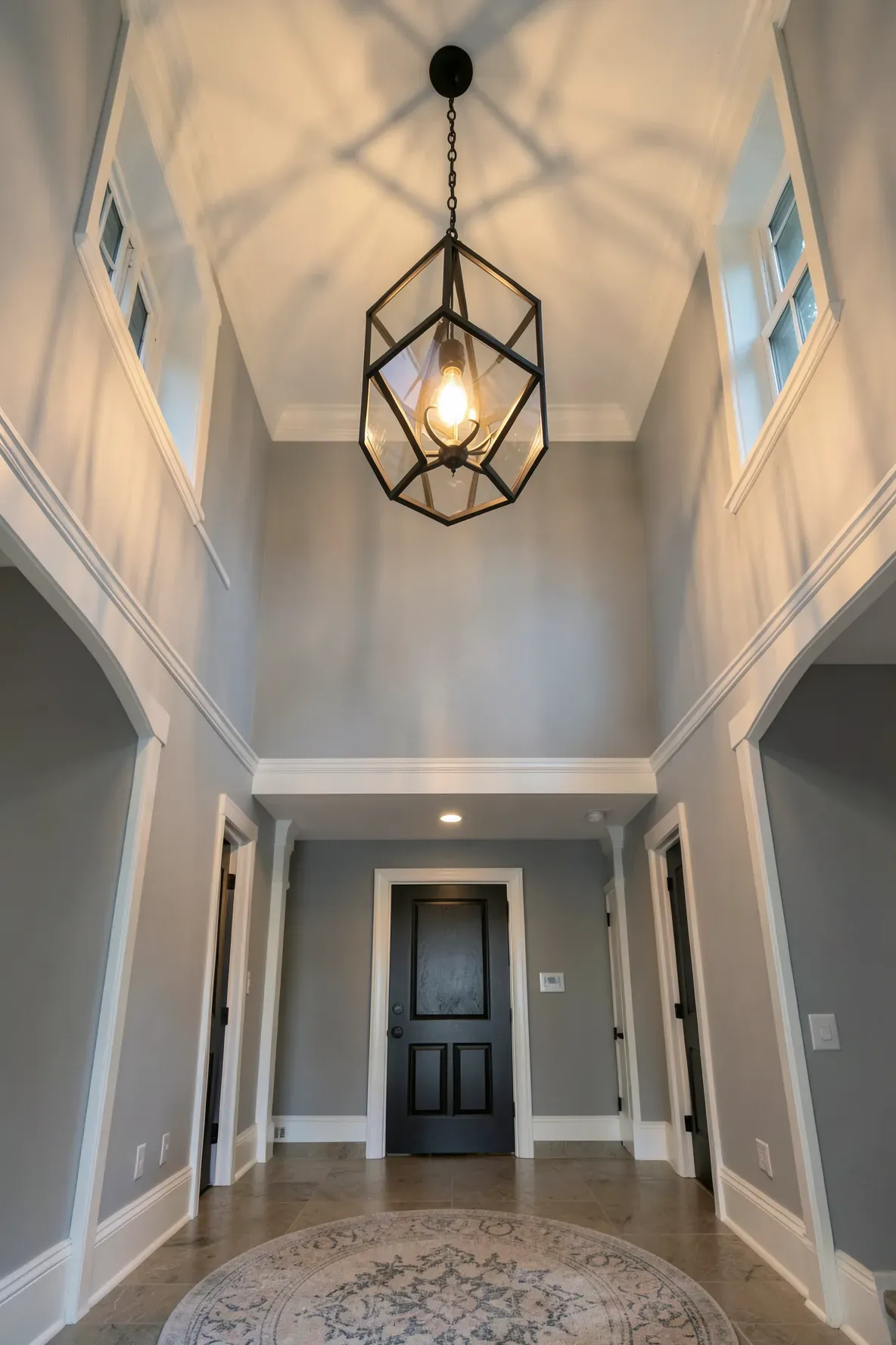 A large black iron lantern pendant light hanging from a high ceiling in a bright entryway.