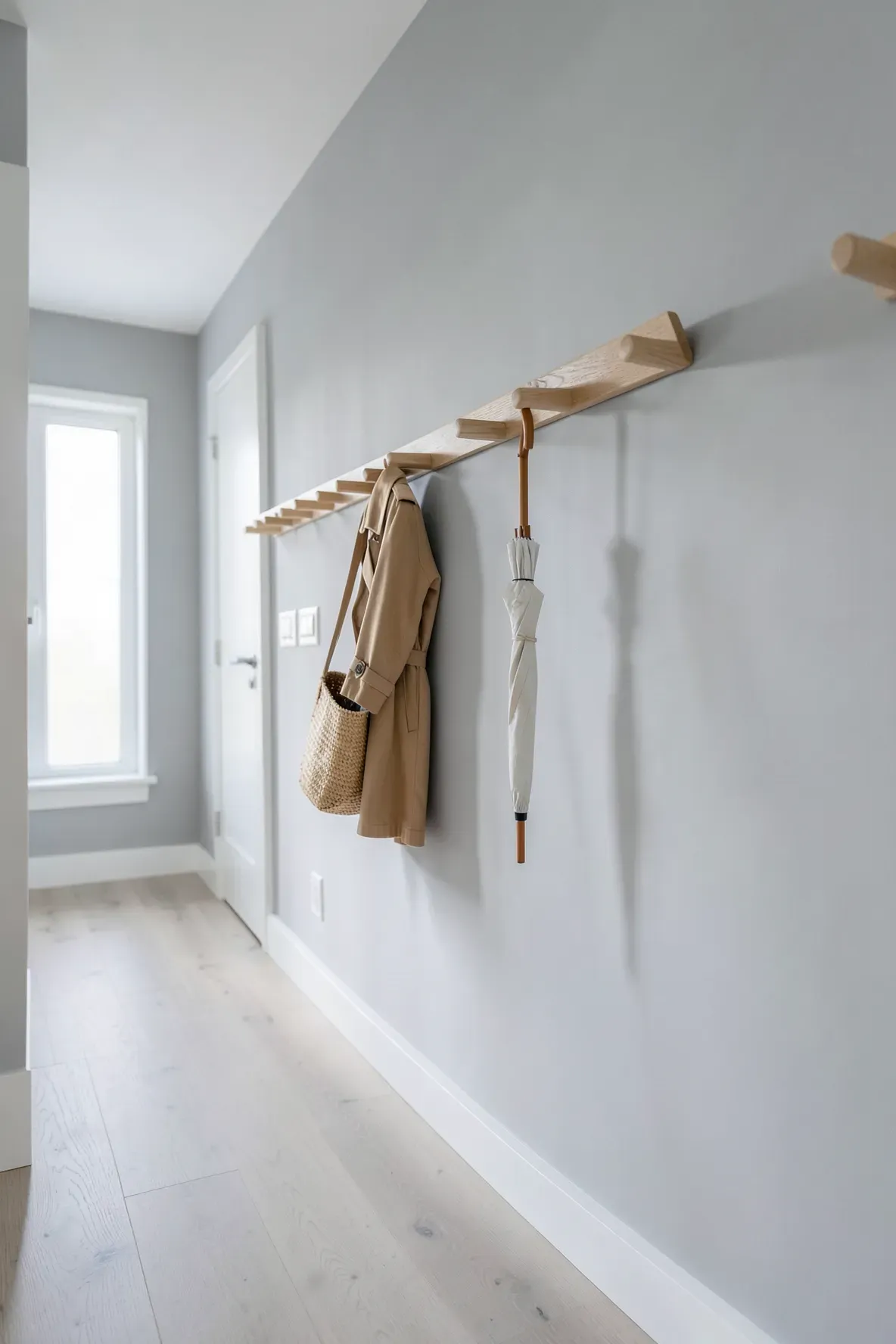 A long wooden peg rail mounted on a light grey hallway wall holding a coat and bag.