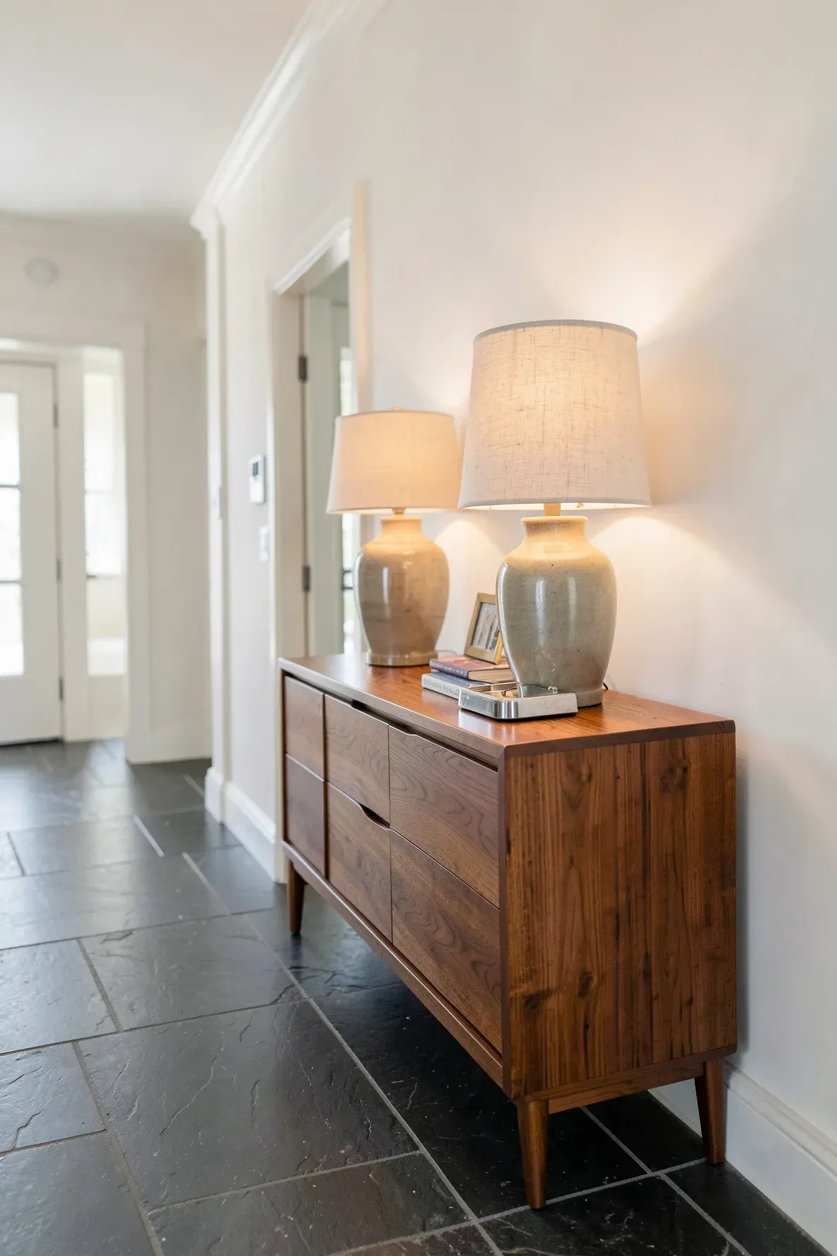 A vintage teak sideboard in a wide hallway styled with a lamp and a mail tray.