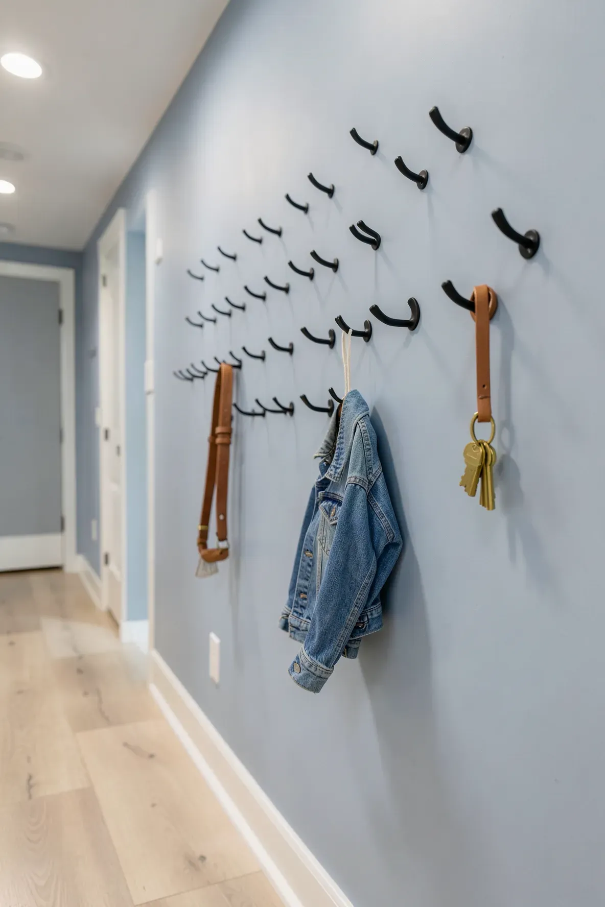 Black decorative wall hooks at different heights on a blue-grey hallway wall.