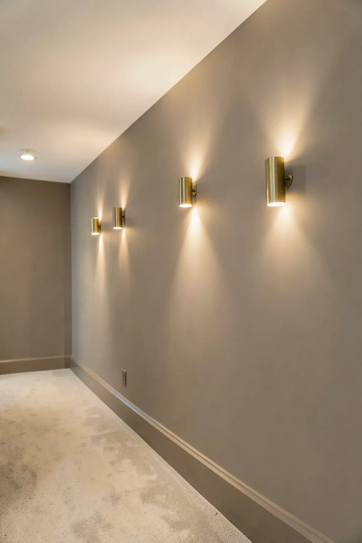A series of elegant brass wall sconces providing warm light in a soft-toned hallway.