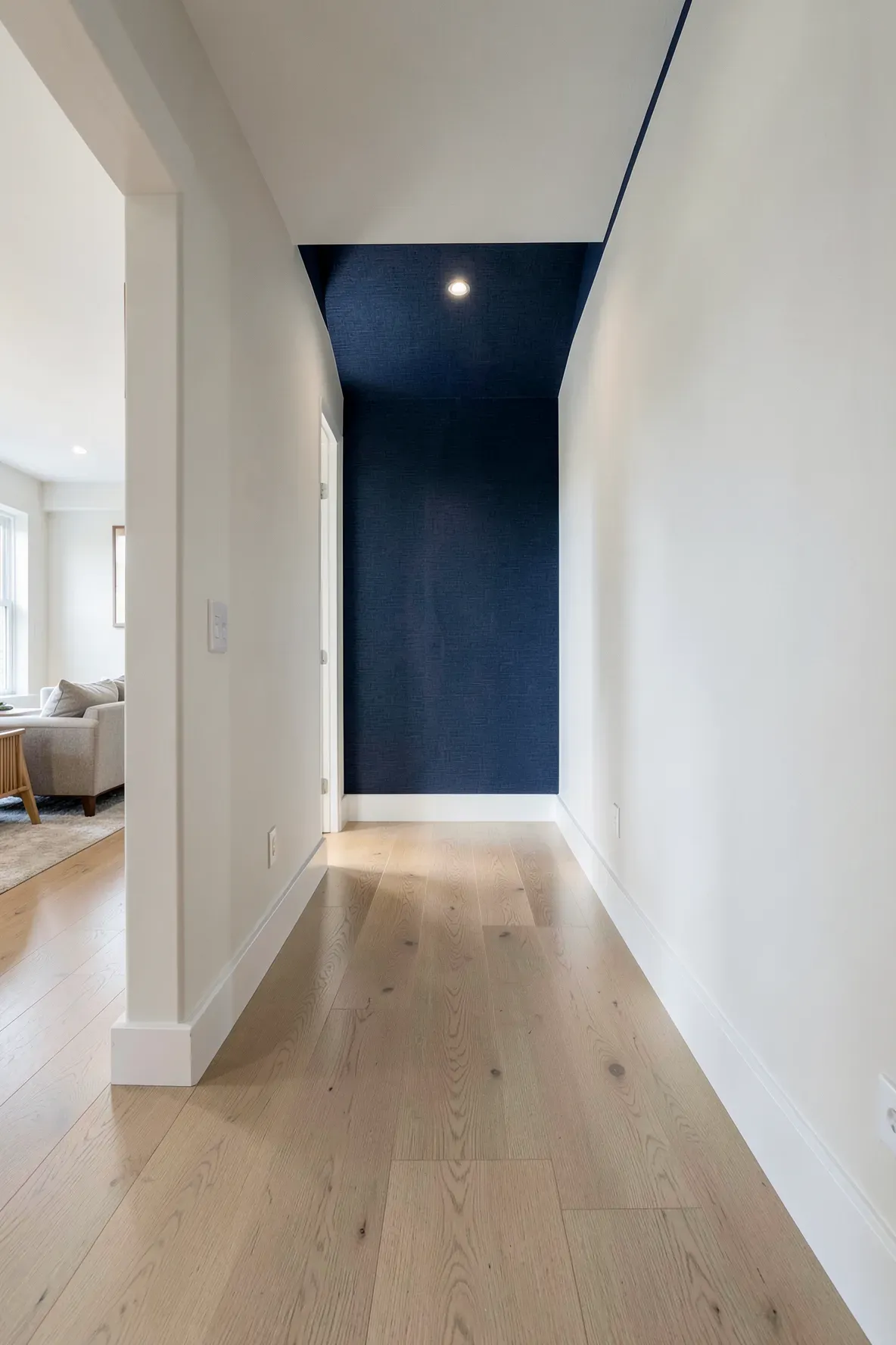 A long hallway with a navy blue grasscloth accent wall at the end and light oak floors.