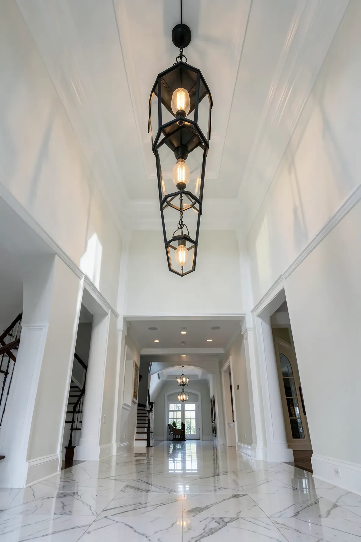 A high-ceilinged hallway with three large black lantern lights hanging in a row.