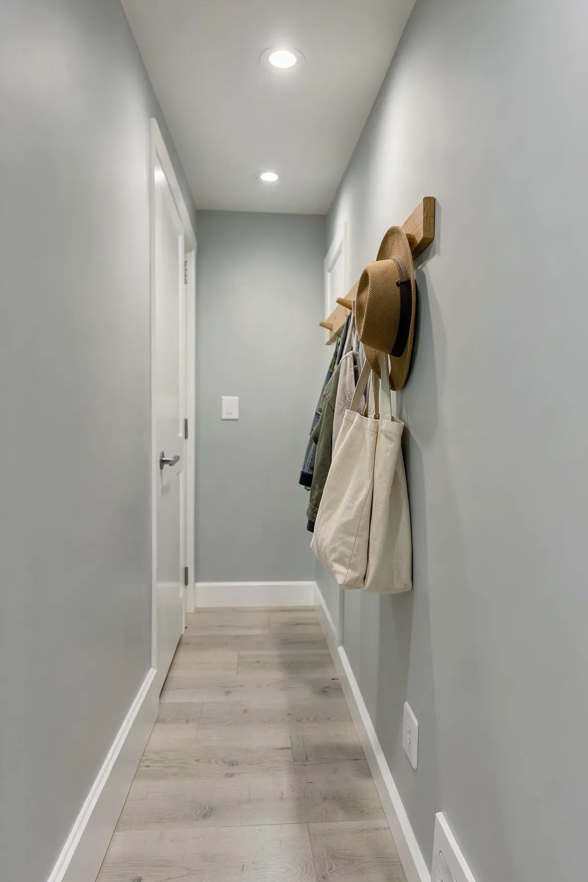 A minimalist grey peg rail on a hallway wall holding a sun hat and a tote bag.