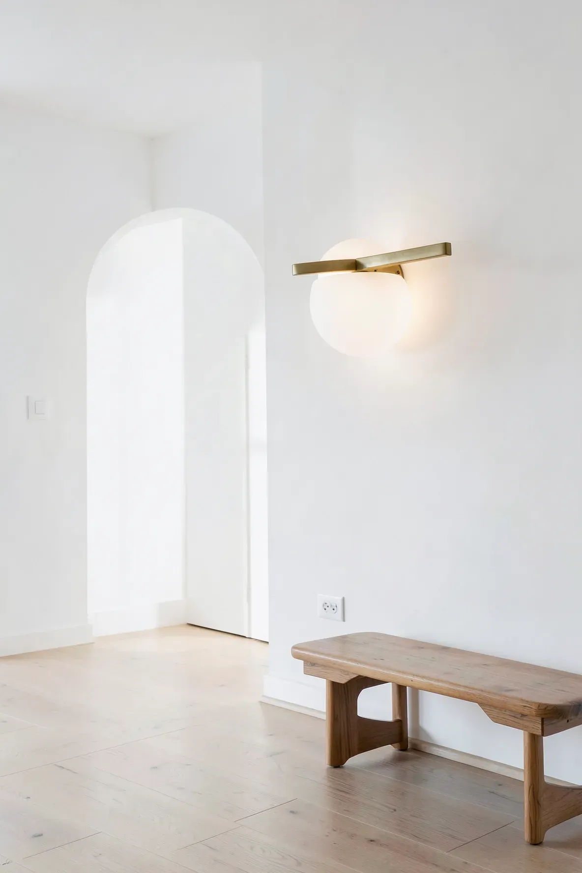 A minimalist antique brass wall light with a white spherical glass globe in a modern hallway.
