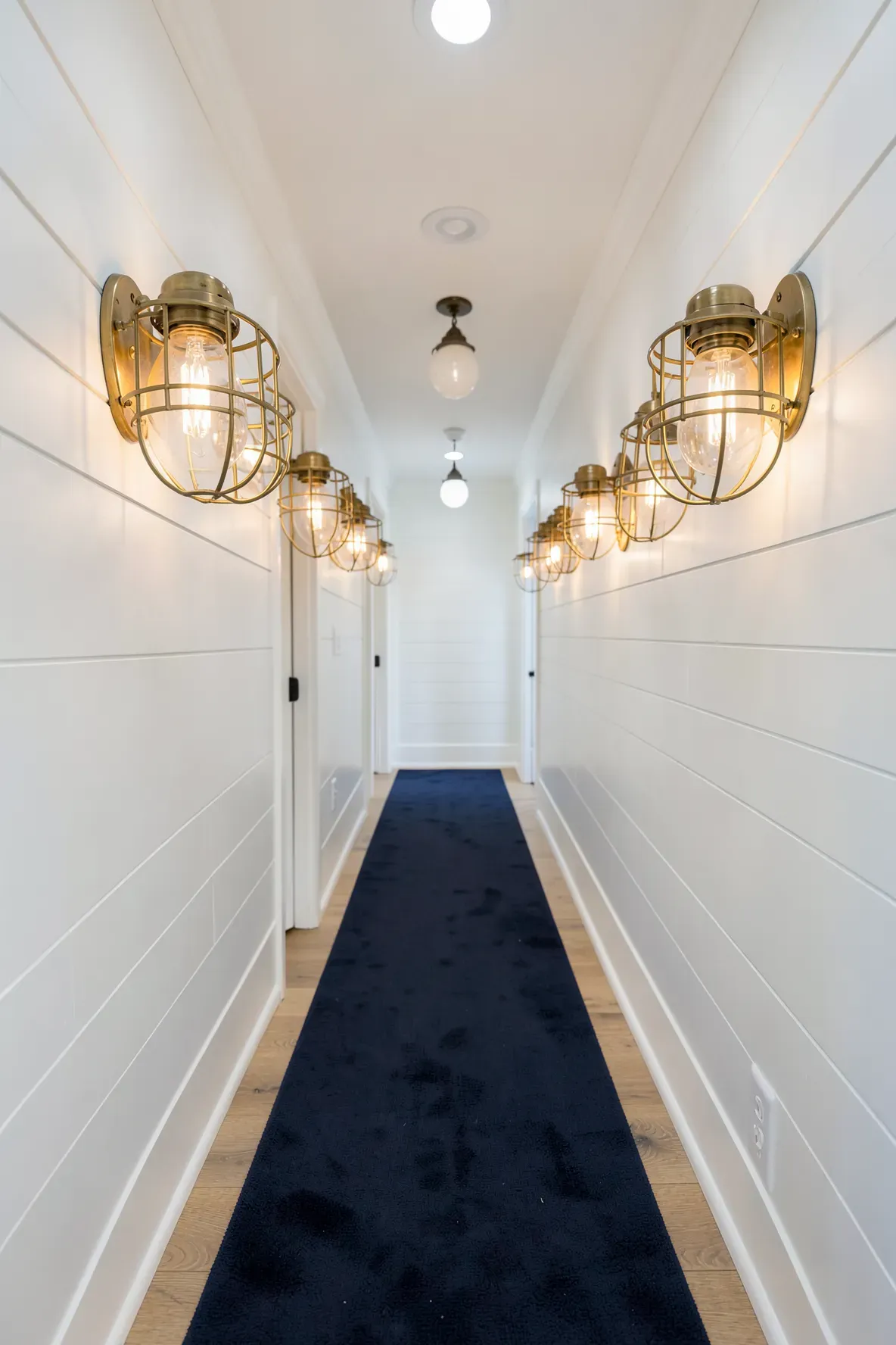 Nautical brass bulkhead lights with metal cages mounted in a white shiplap hallway.