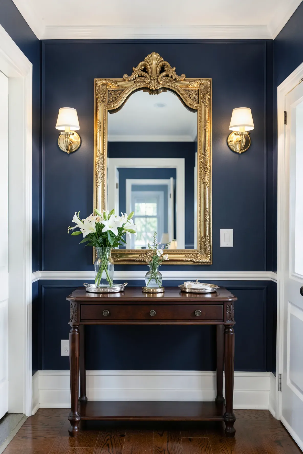 Symmetrical polished gold wall lights framing a large mirror in a navy blue entryway.