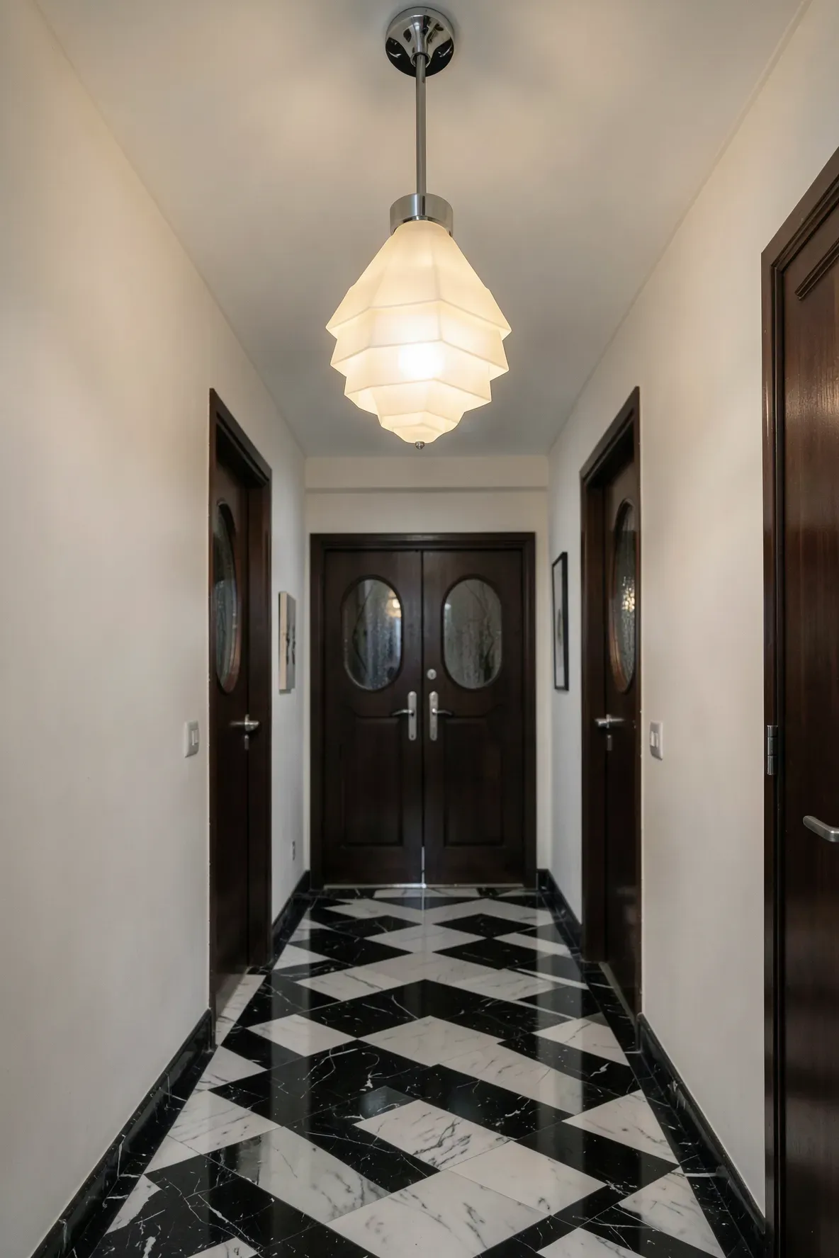 A geometric Art Deco milk glass pendant light hanging in a symmetrical black and white marble hallway.