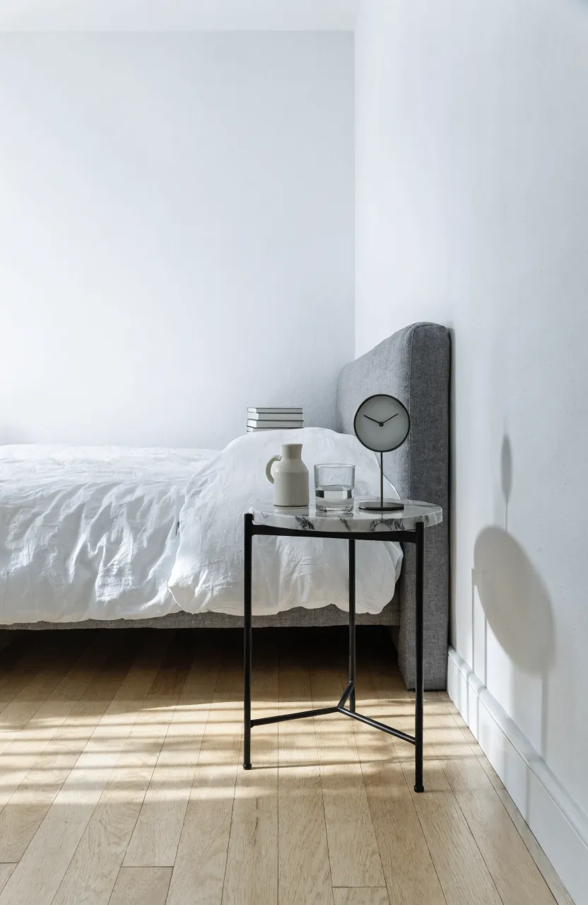 A narrow round nightstand next to a bed positioned in a room corner.