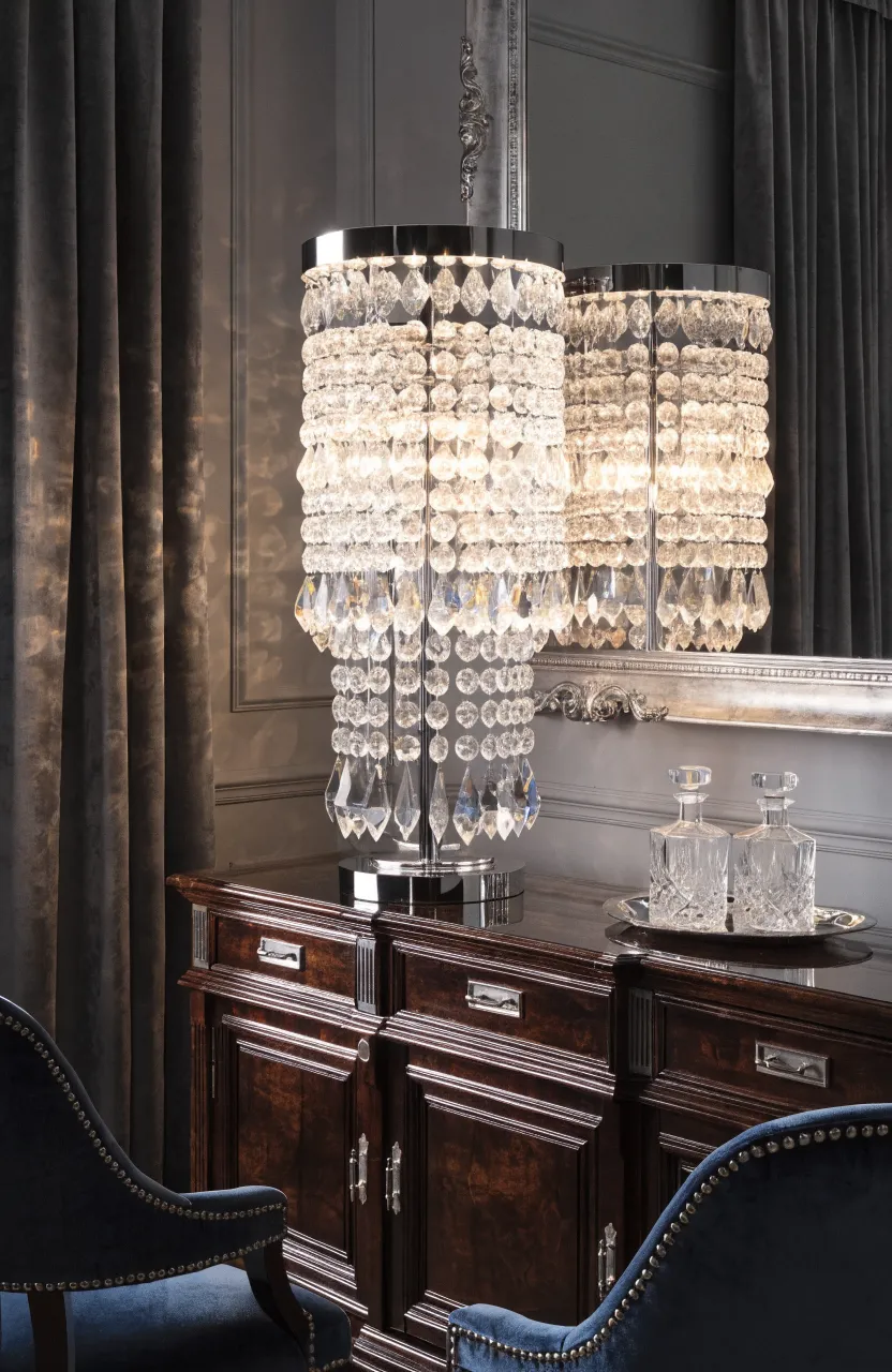 A crystal table lamp with cascading droplets glowing on a dark wood sideboard in a formal room.