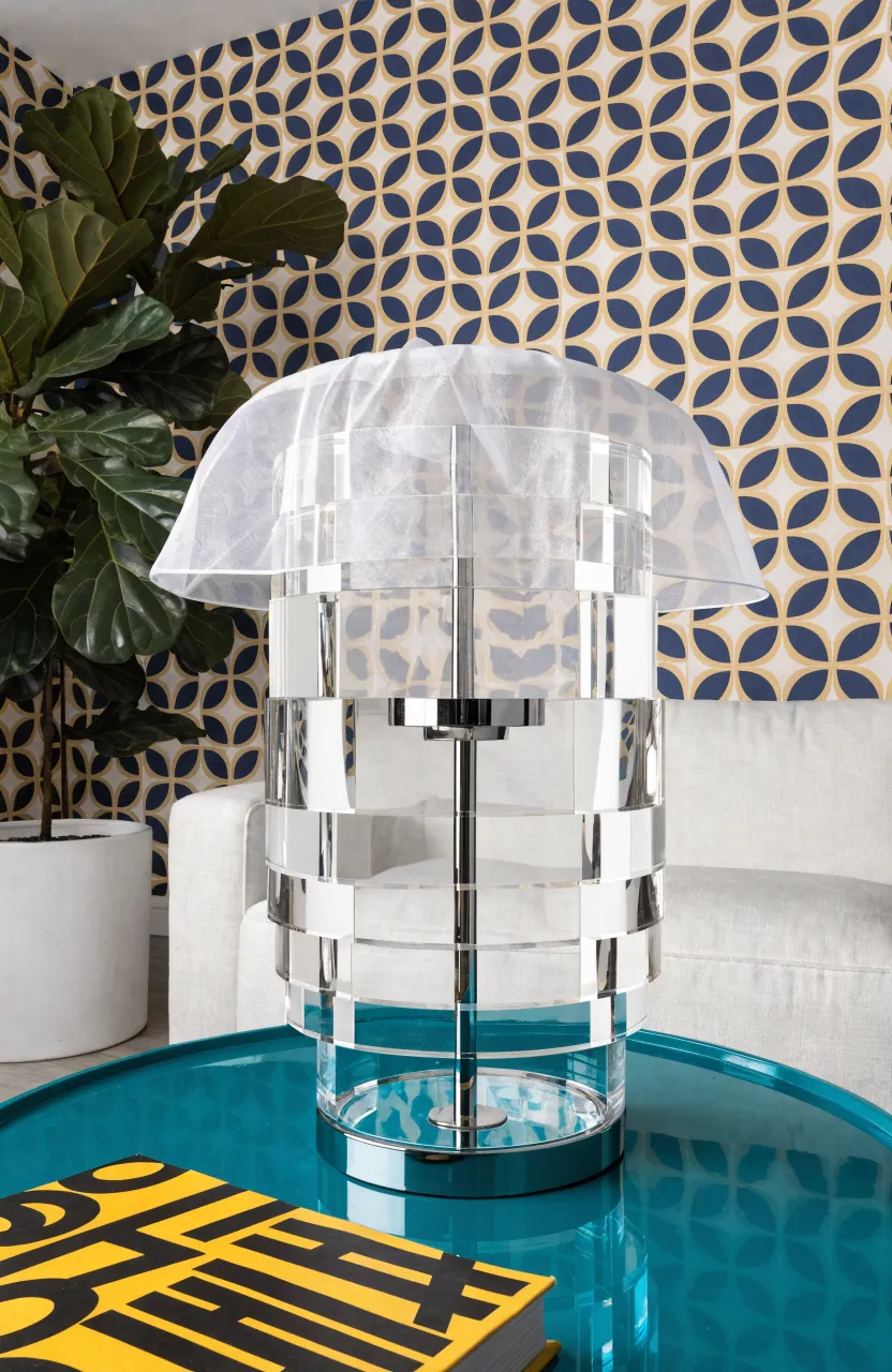 A transparent layered acrylic lamp on a teal table against geometric wallpaper.