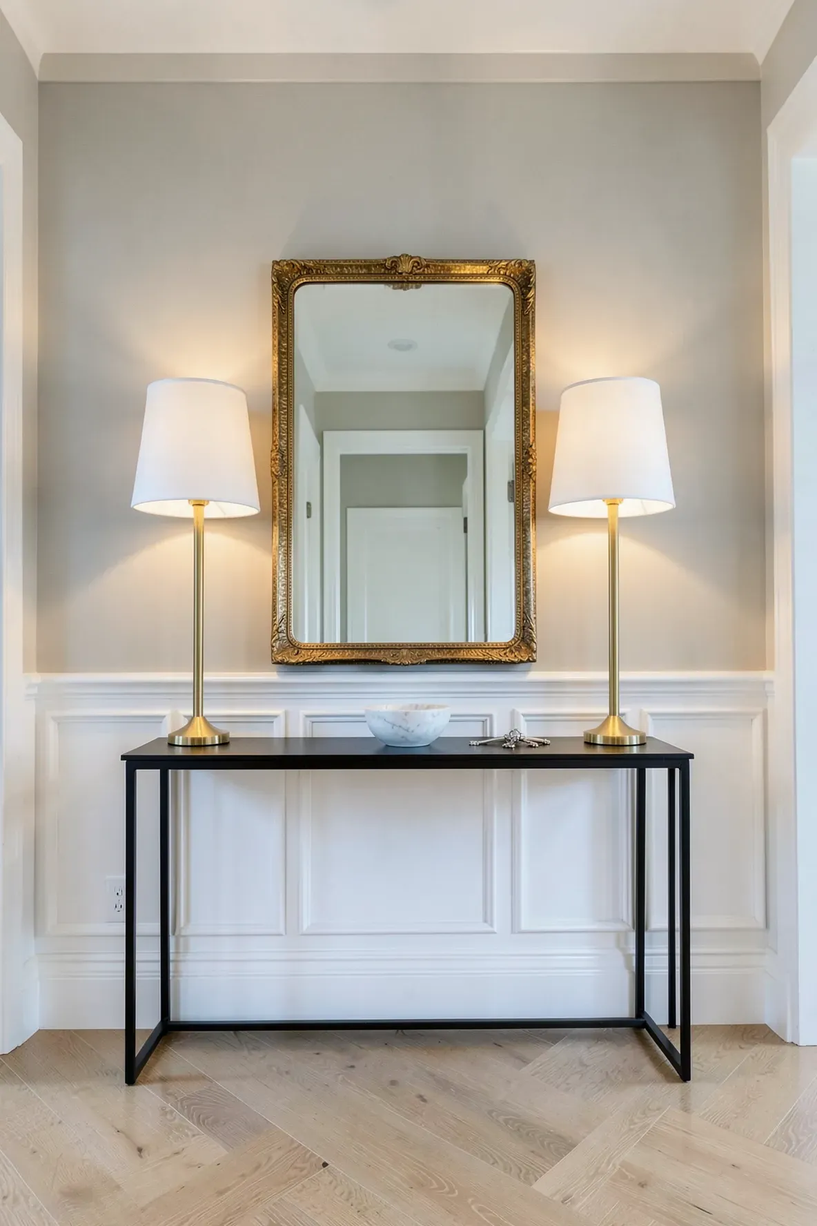 Symmetrical tall brass lamps framing a large mirror on a black console table in a bright entryway.