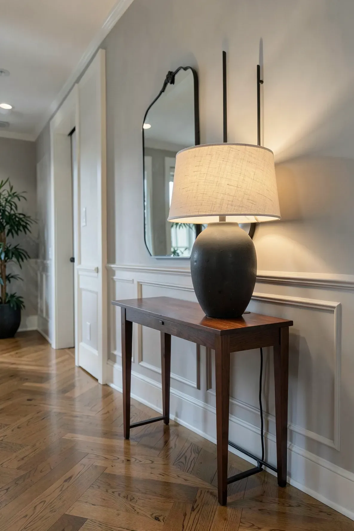 A large charcoal ceramic lamp perfectly scaled on a narrow mahogany console table in a hallway.