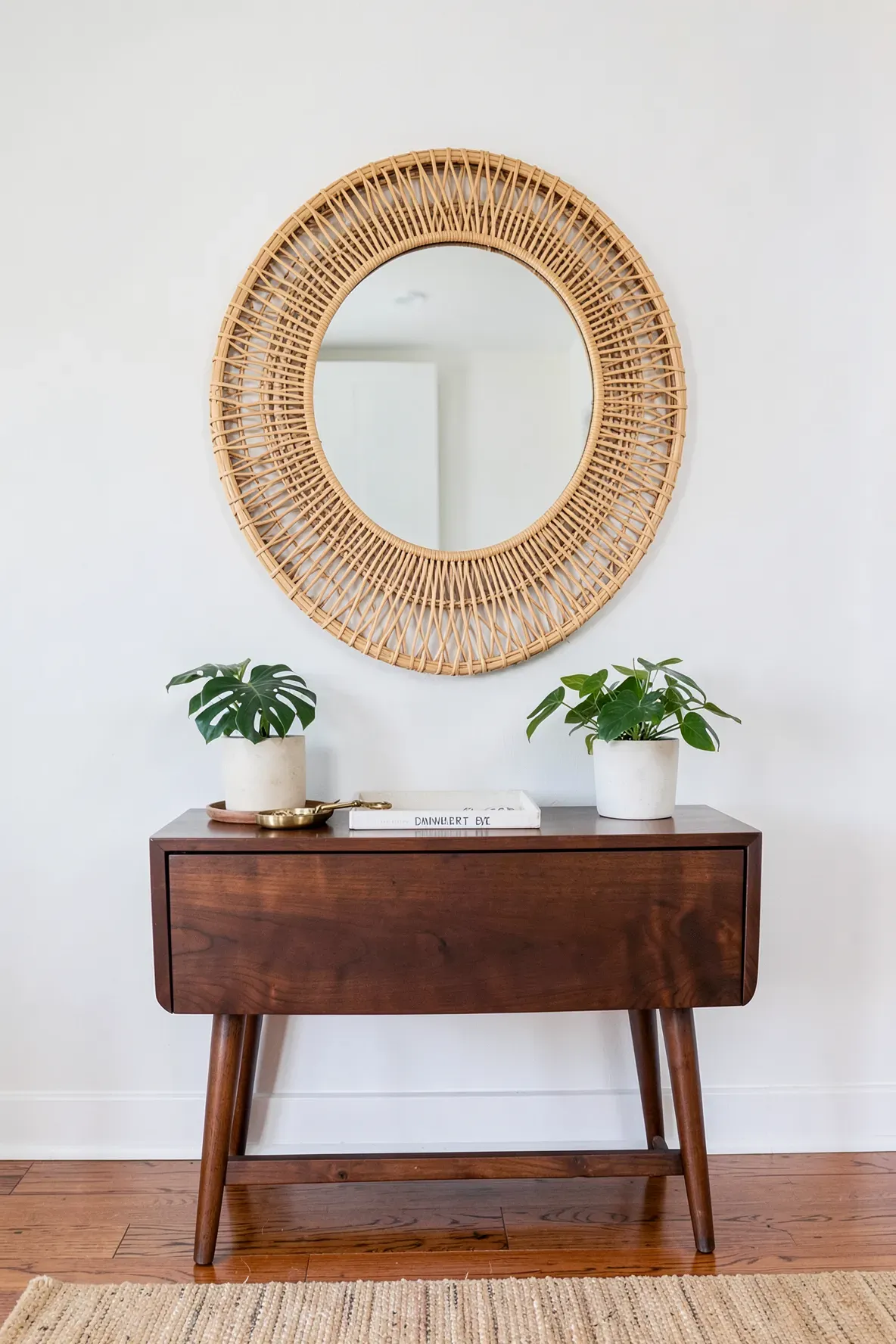 A large round rattan mirror perfectly centered above a walnut console table in an entryway.